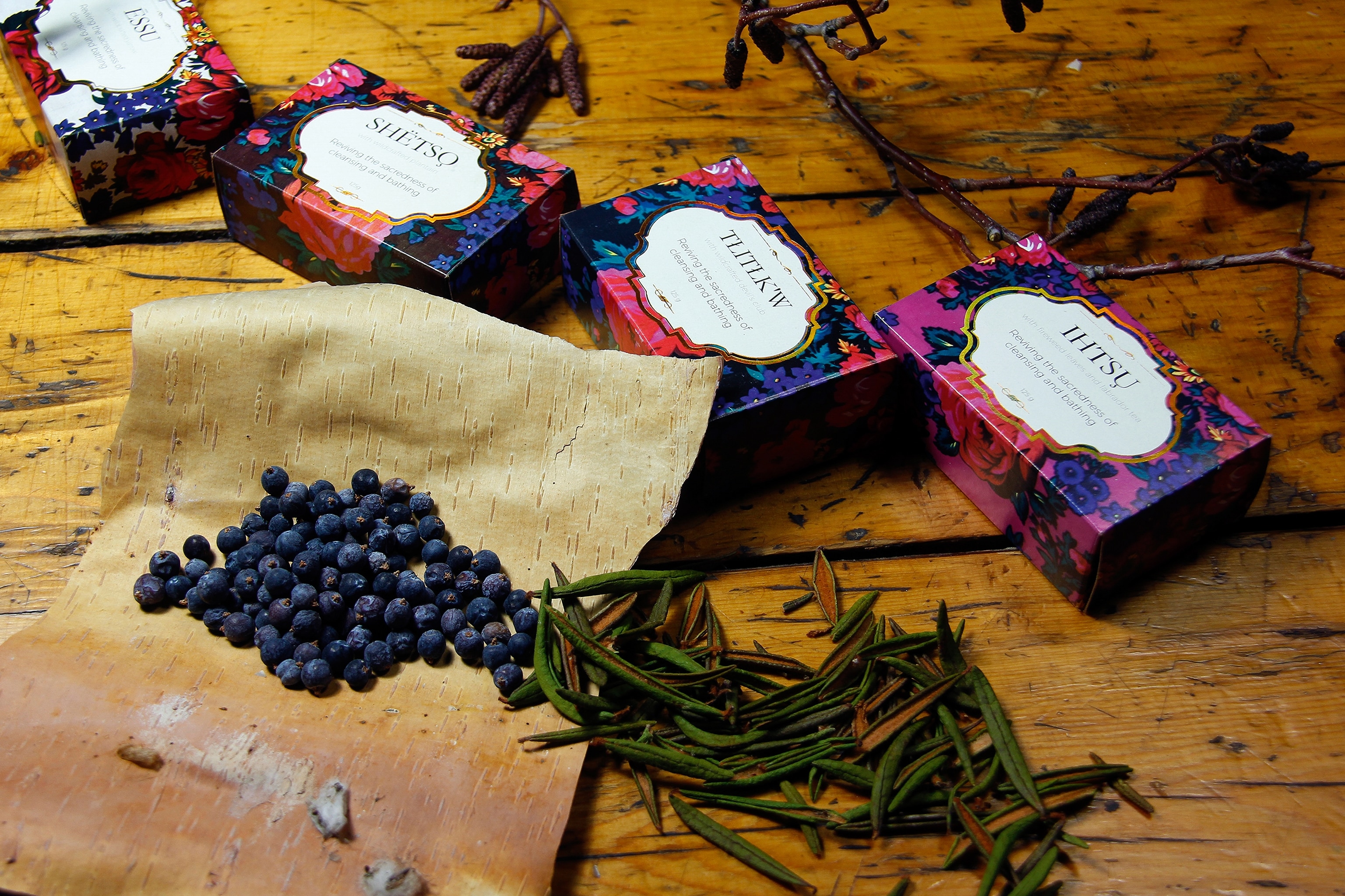 A quartett of packaged soap bars is lying next to berries and rosemary.
