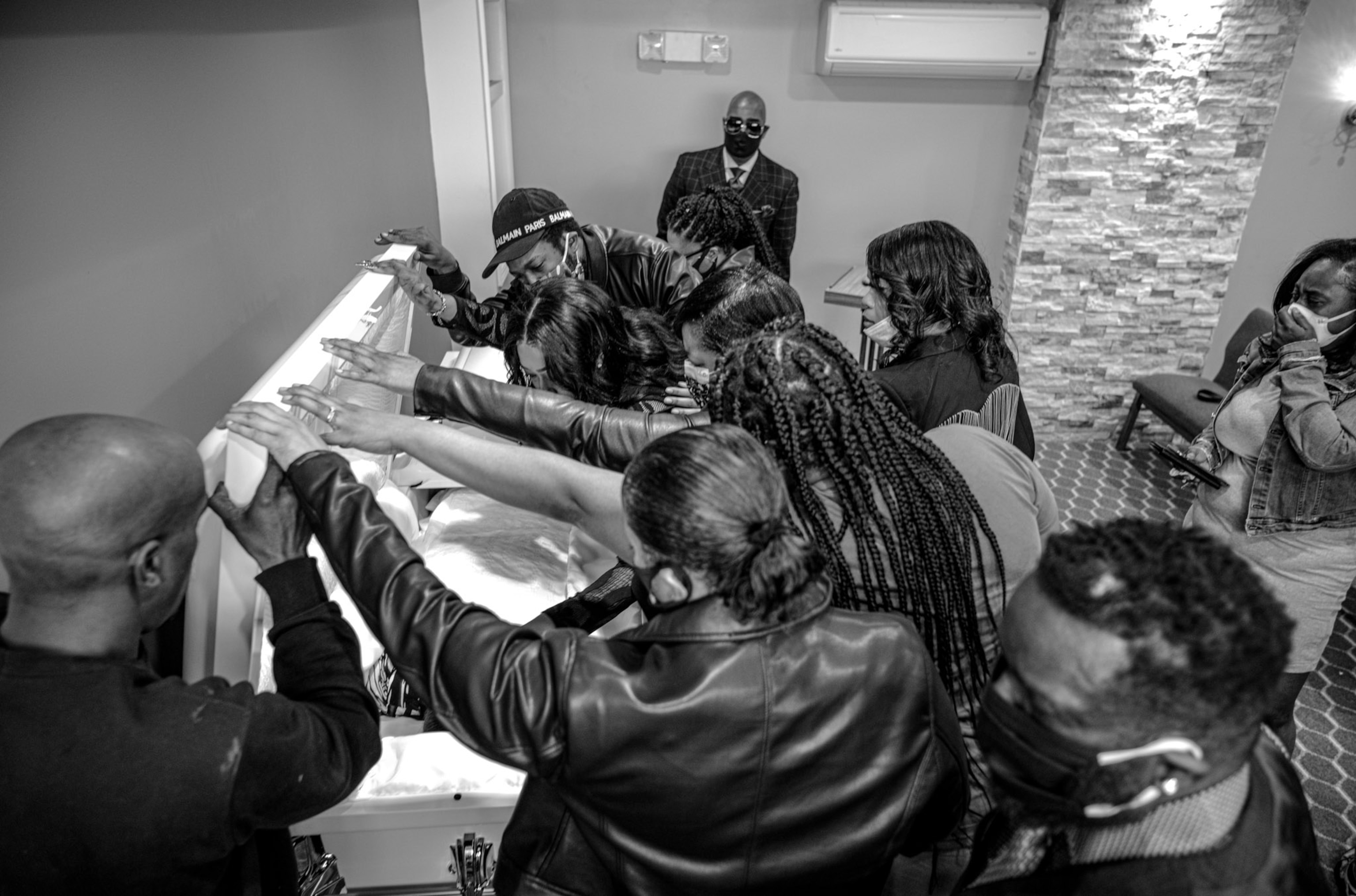 multiple people with their hands on the open half of a casket, looking into the casket