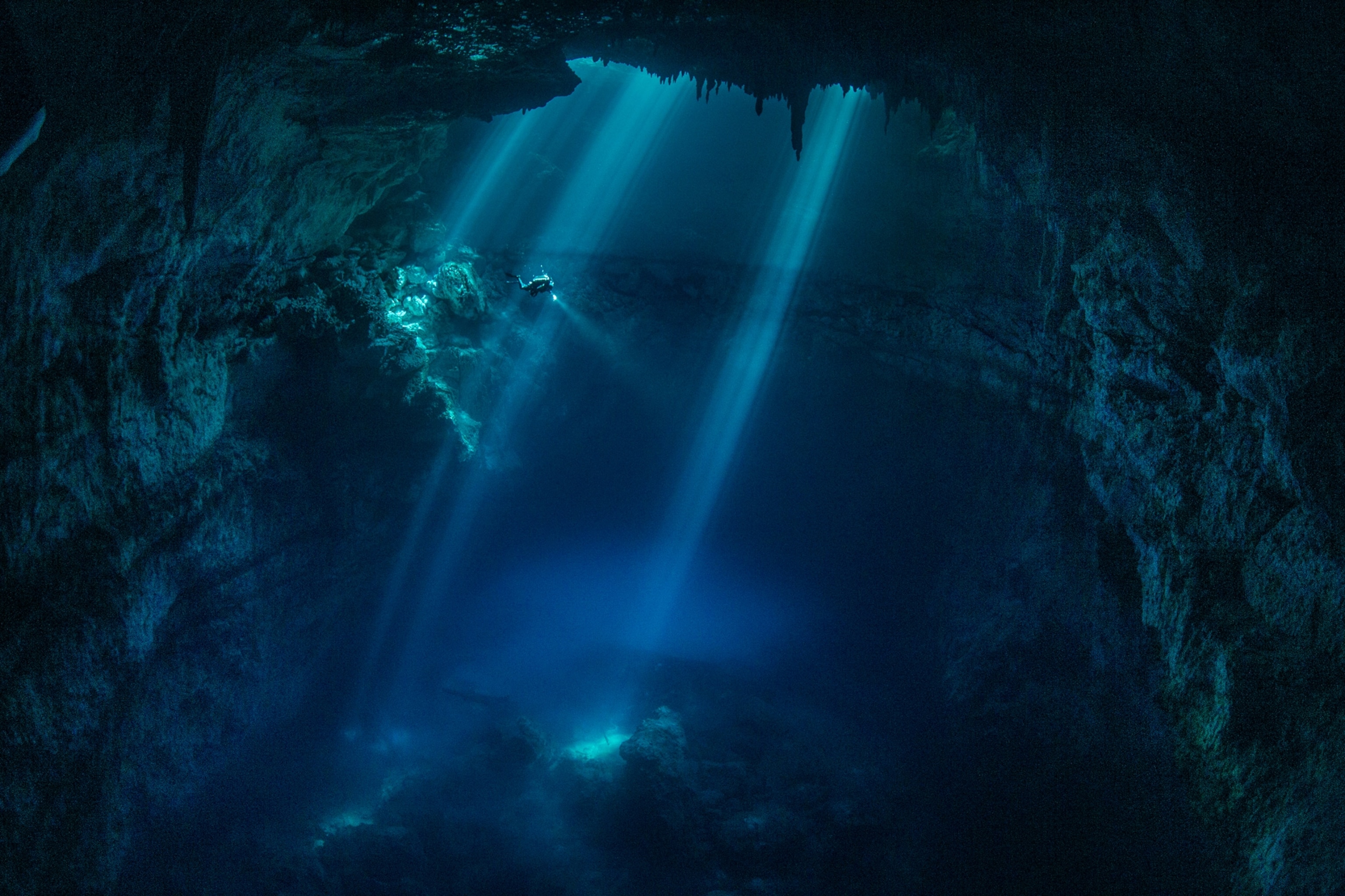 The diver in dark blue water in the rays of light from above.