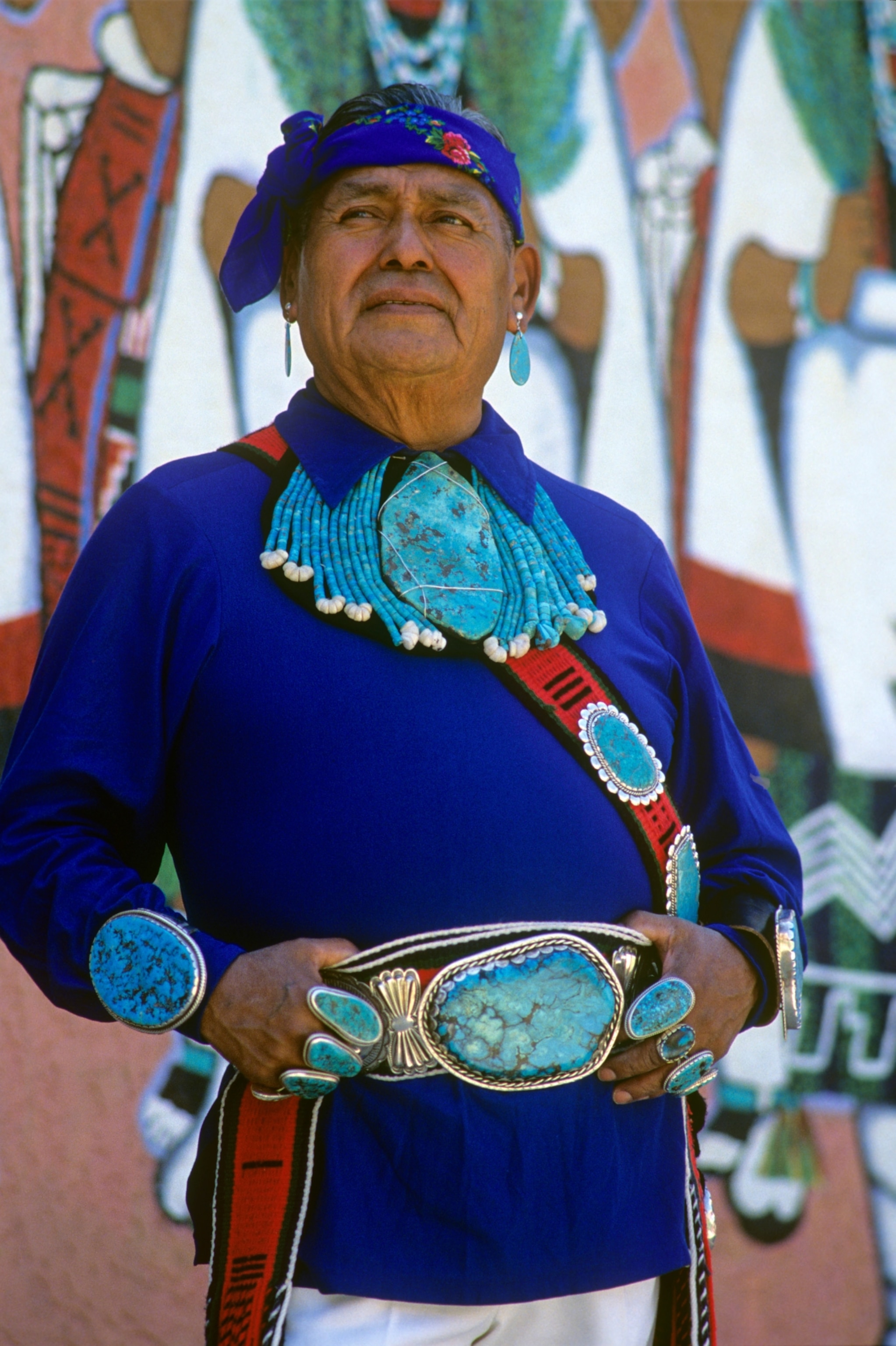 Native man stands tall covered in large discs of turquoise
