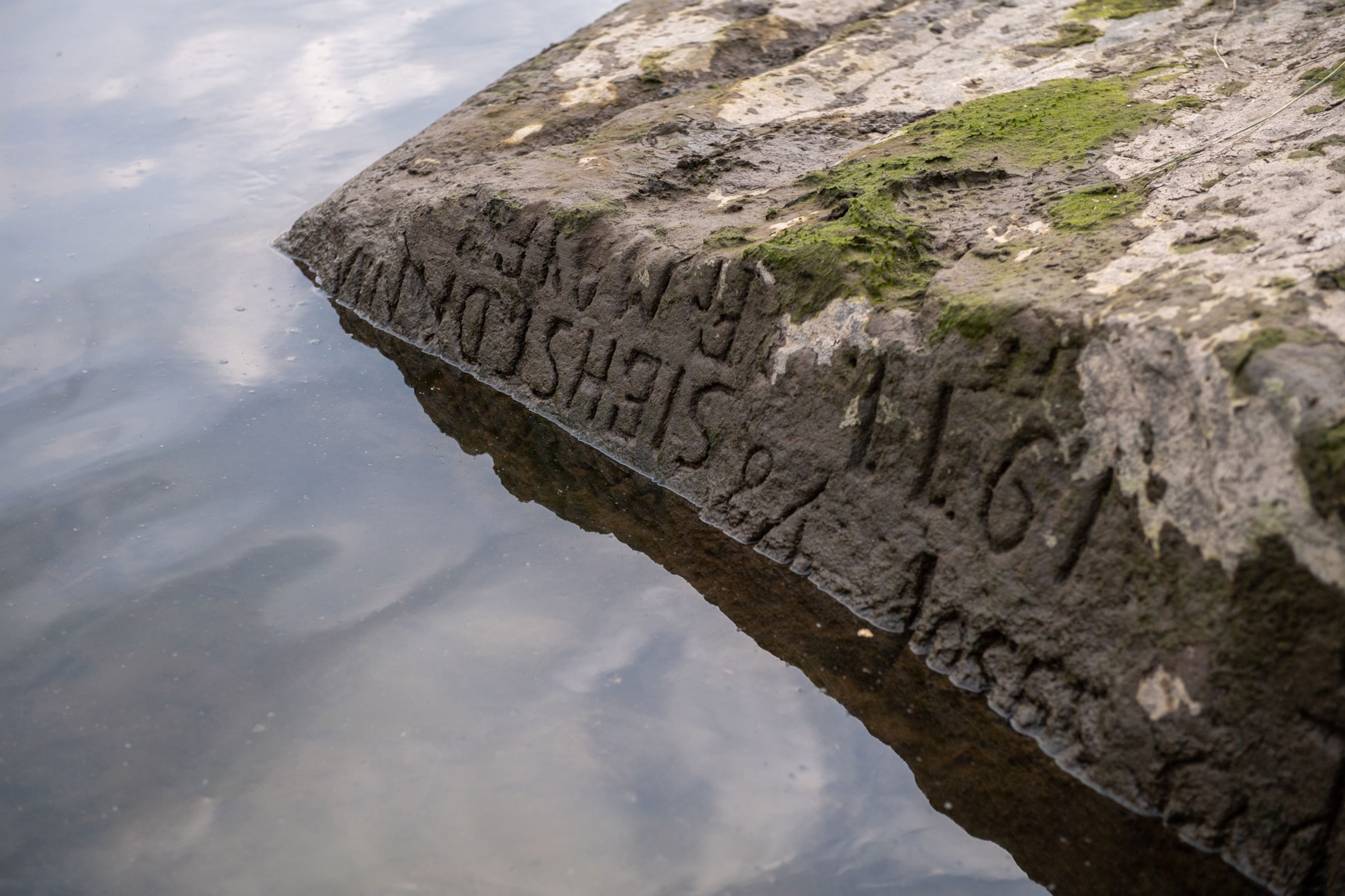 a stone at the edge of a waterline with words etched into it