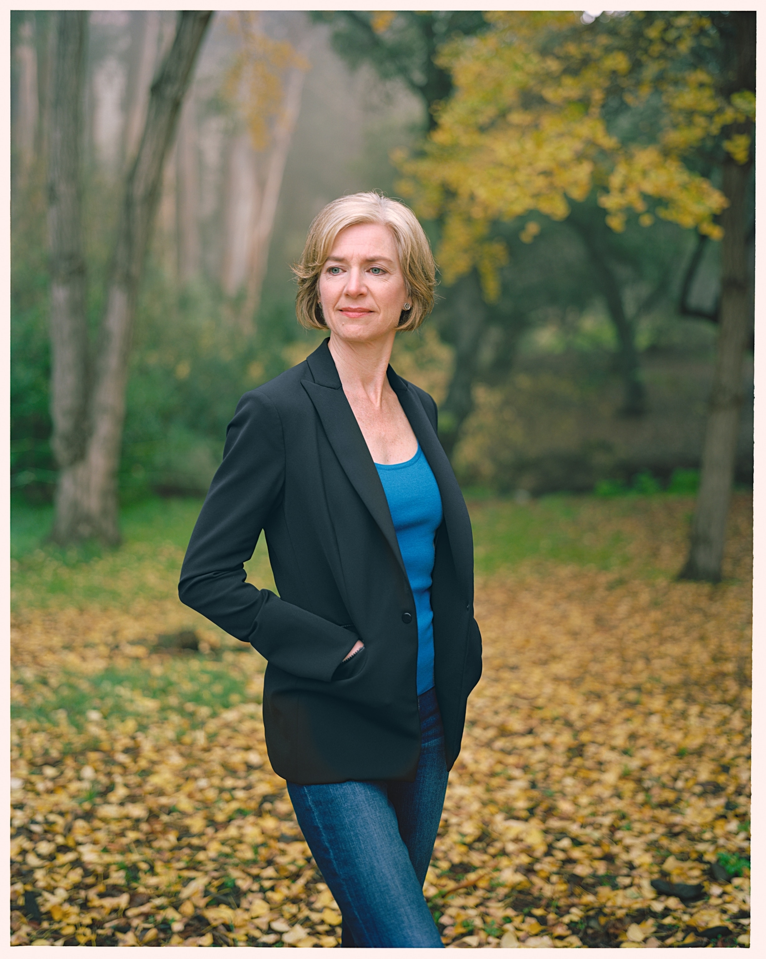 a woman in blue jeans with her hands in the jacket pockets in the autumn garden.
