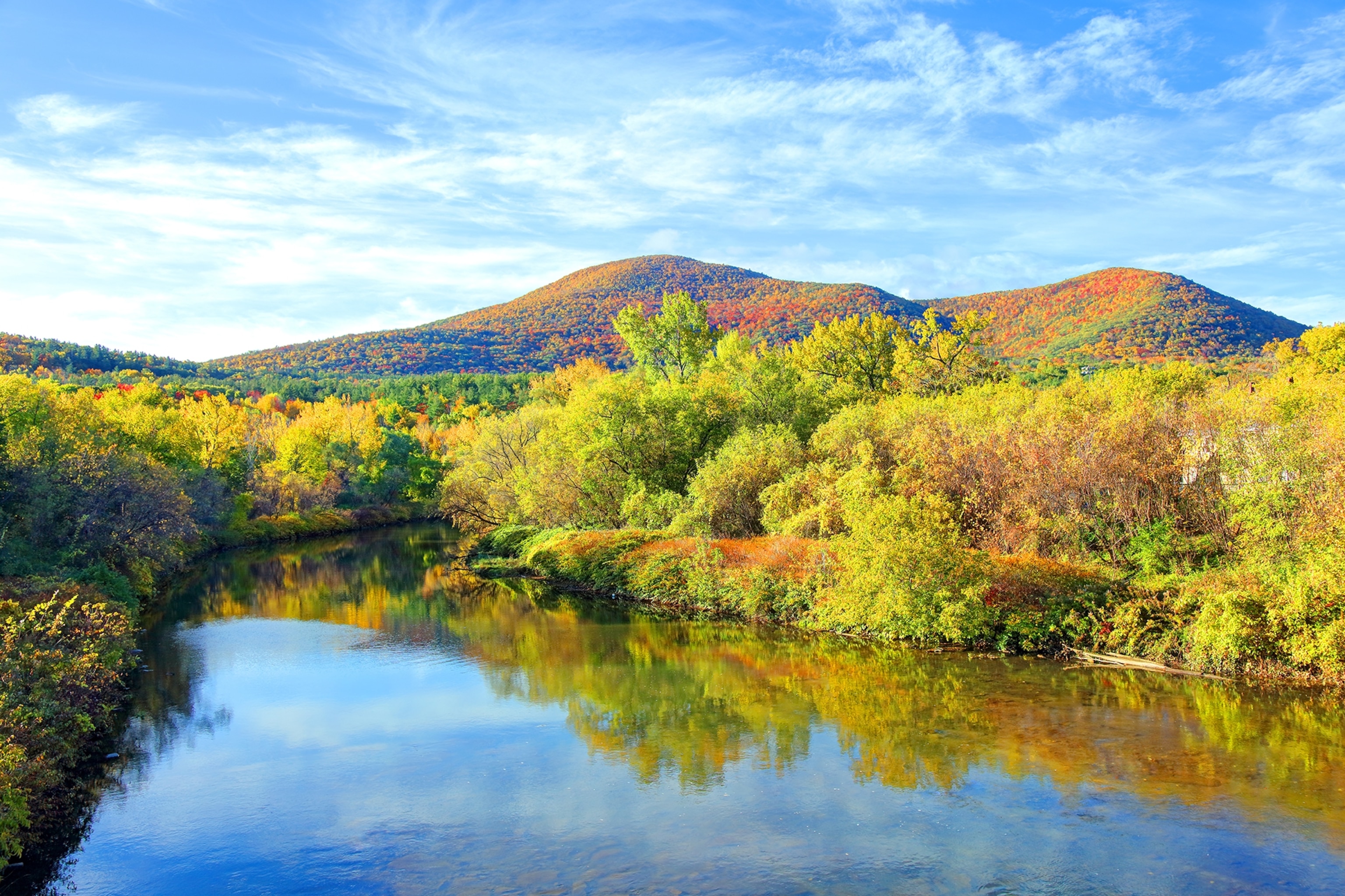 Mountains in the fall with autumn coloured trees and a river running in the foreground reflecting the trees