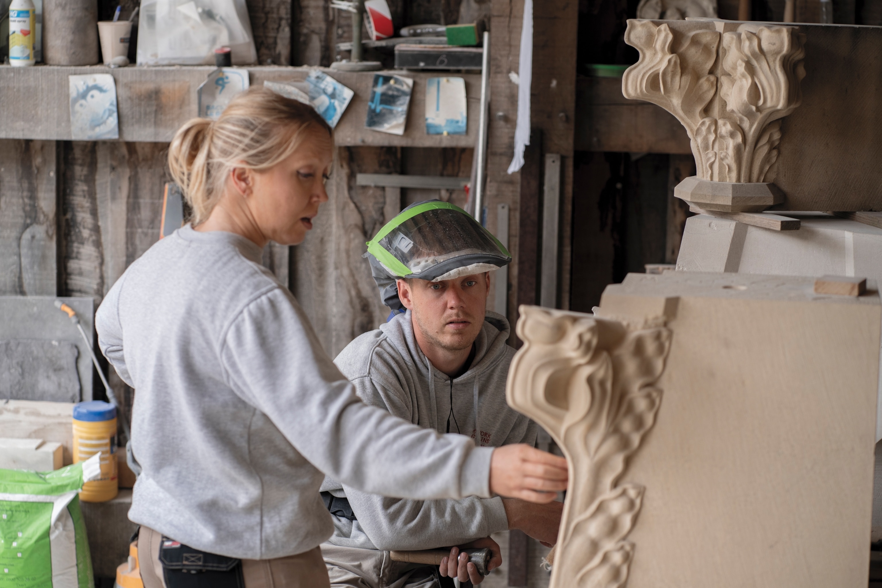 Man with lifted up face shield and women discussing the stone object they are looking at.