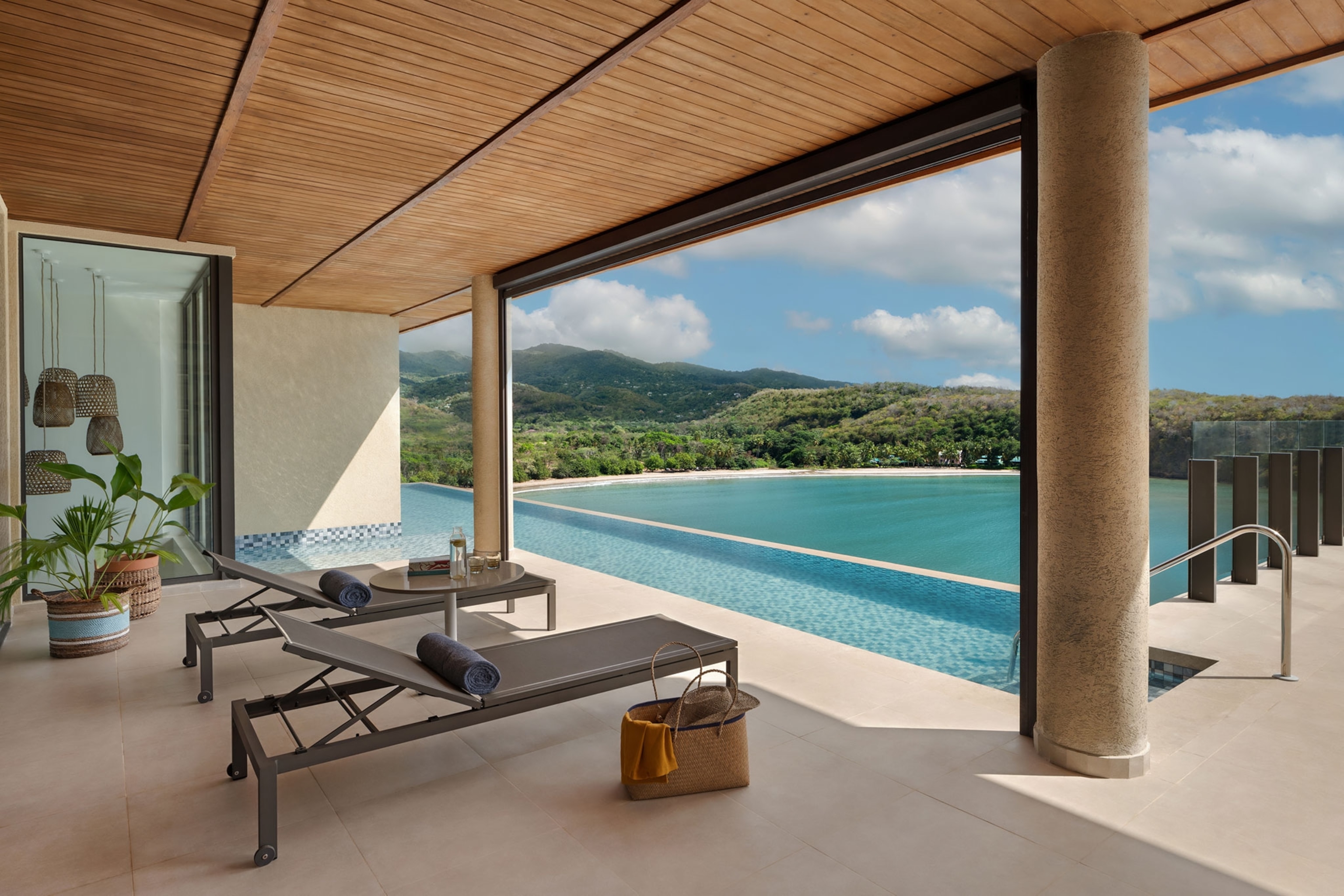 Poolside view from behind two lounge chairs. Green, tree covered mountains in the distance.
