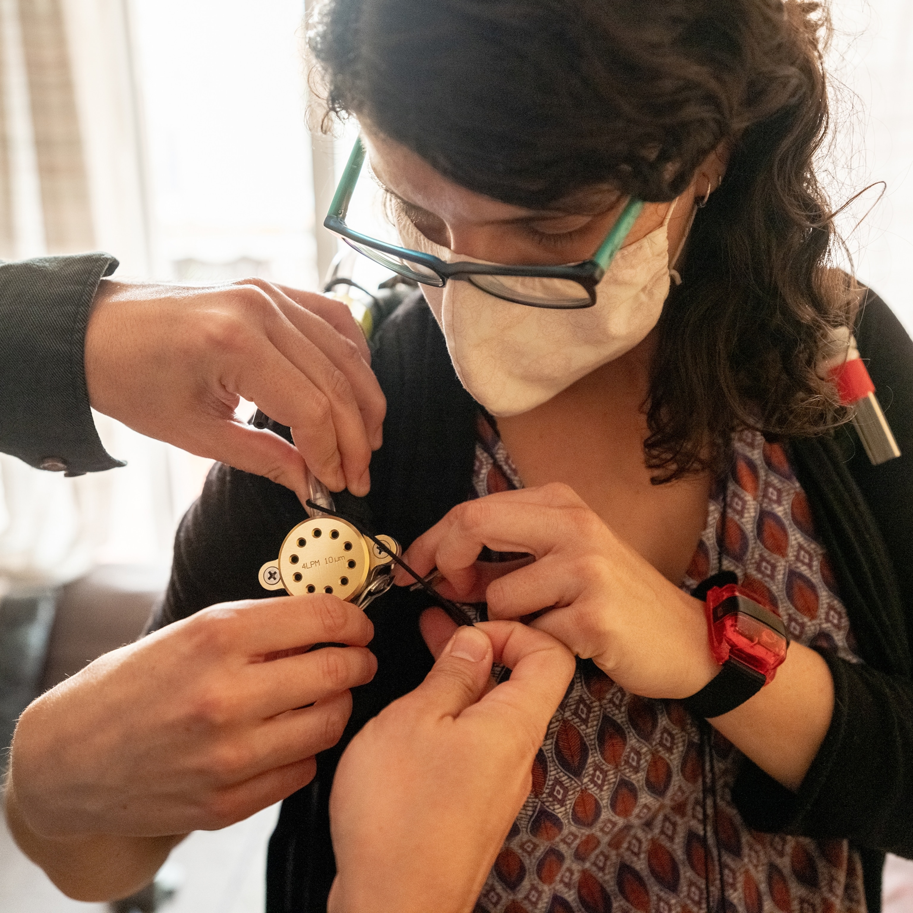 Picture of woman in face mask affixing a small devise on her shoulder.