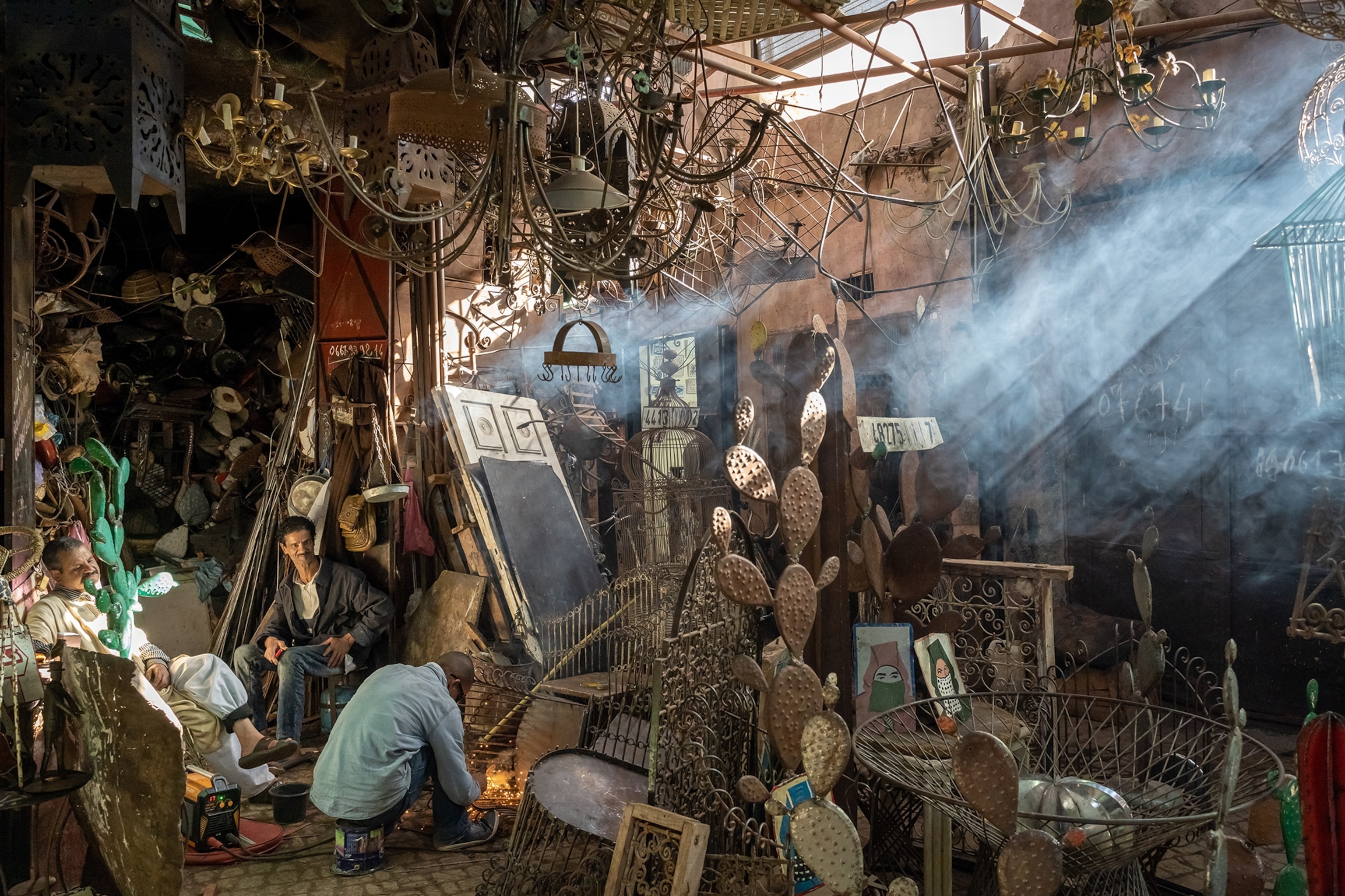 A souk in Morocco. Intricate blacksmith work is placed in every corner of a shopfront, with the blacksmiths smiling and chatting as they work.