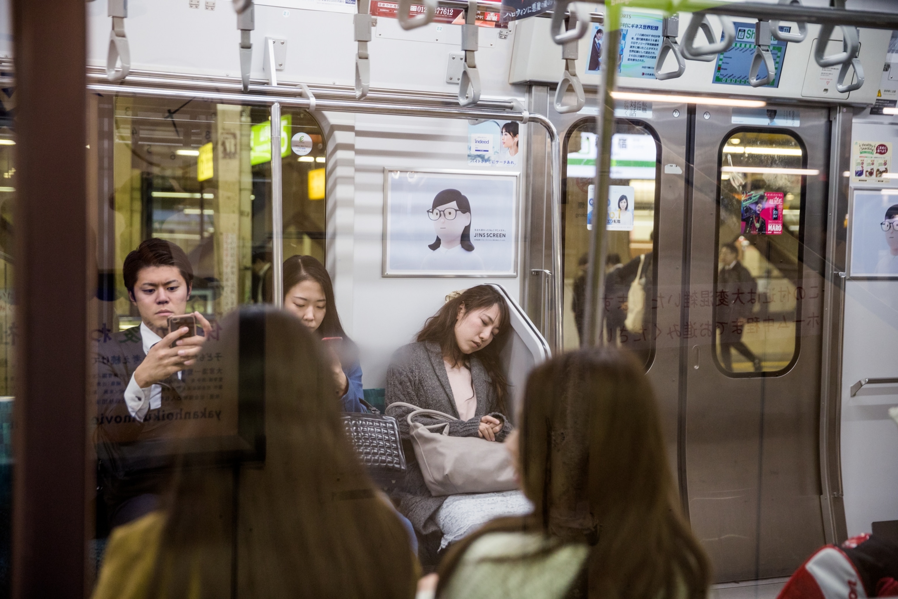 people on the subway using their cellphones next to one woman resting her head on a wall