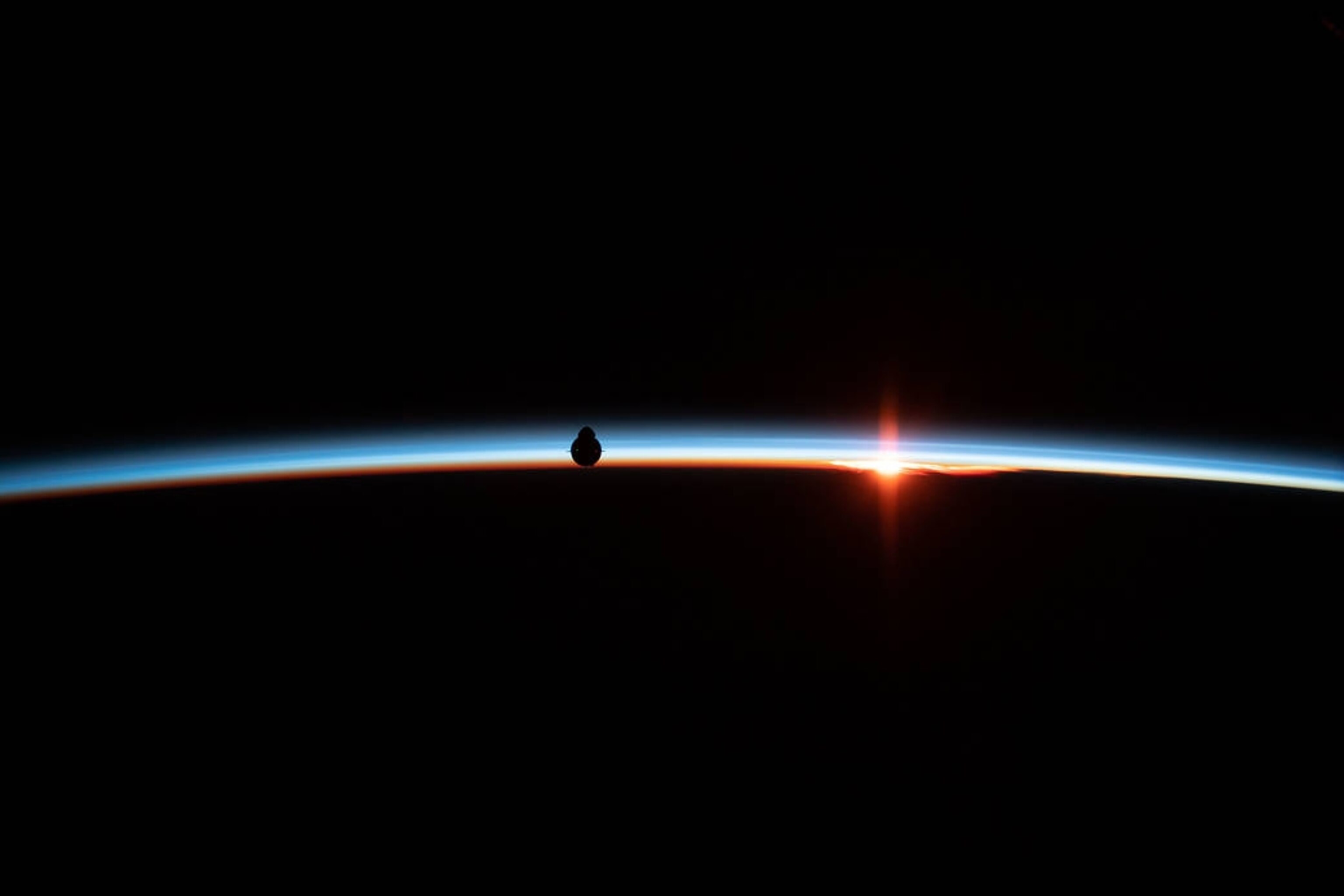 the uncrewed SpaceX Crew Dragon spacecraft is silhouetted against the Earth's horizon