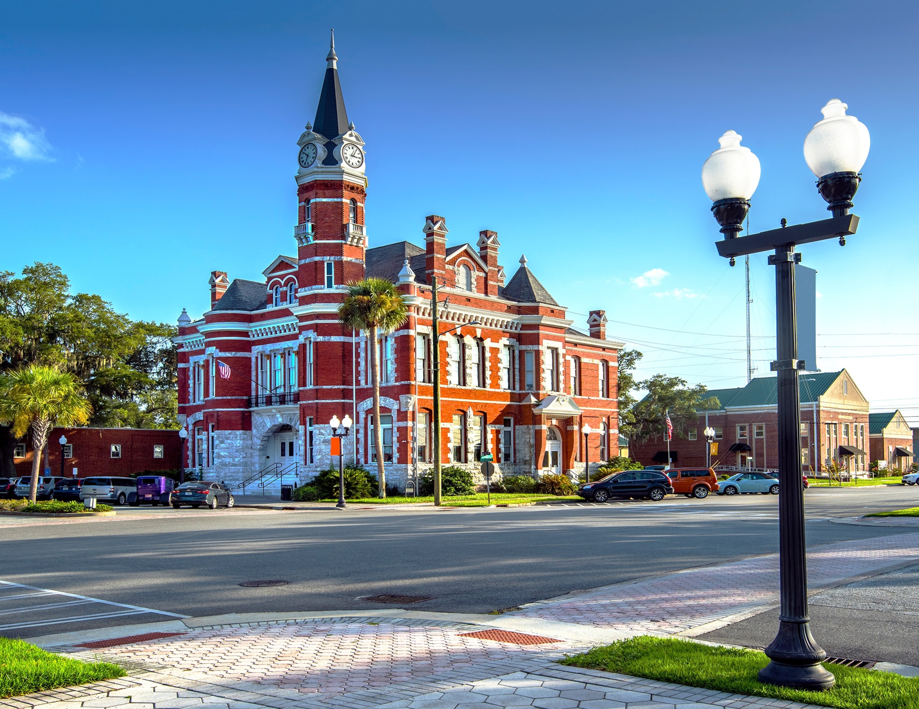 A Building with brick details and a clock face sits on a corner under a blue sky.