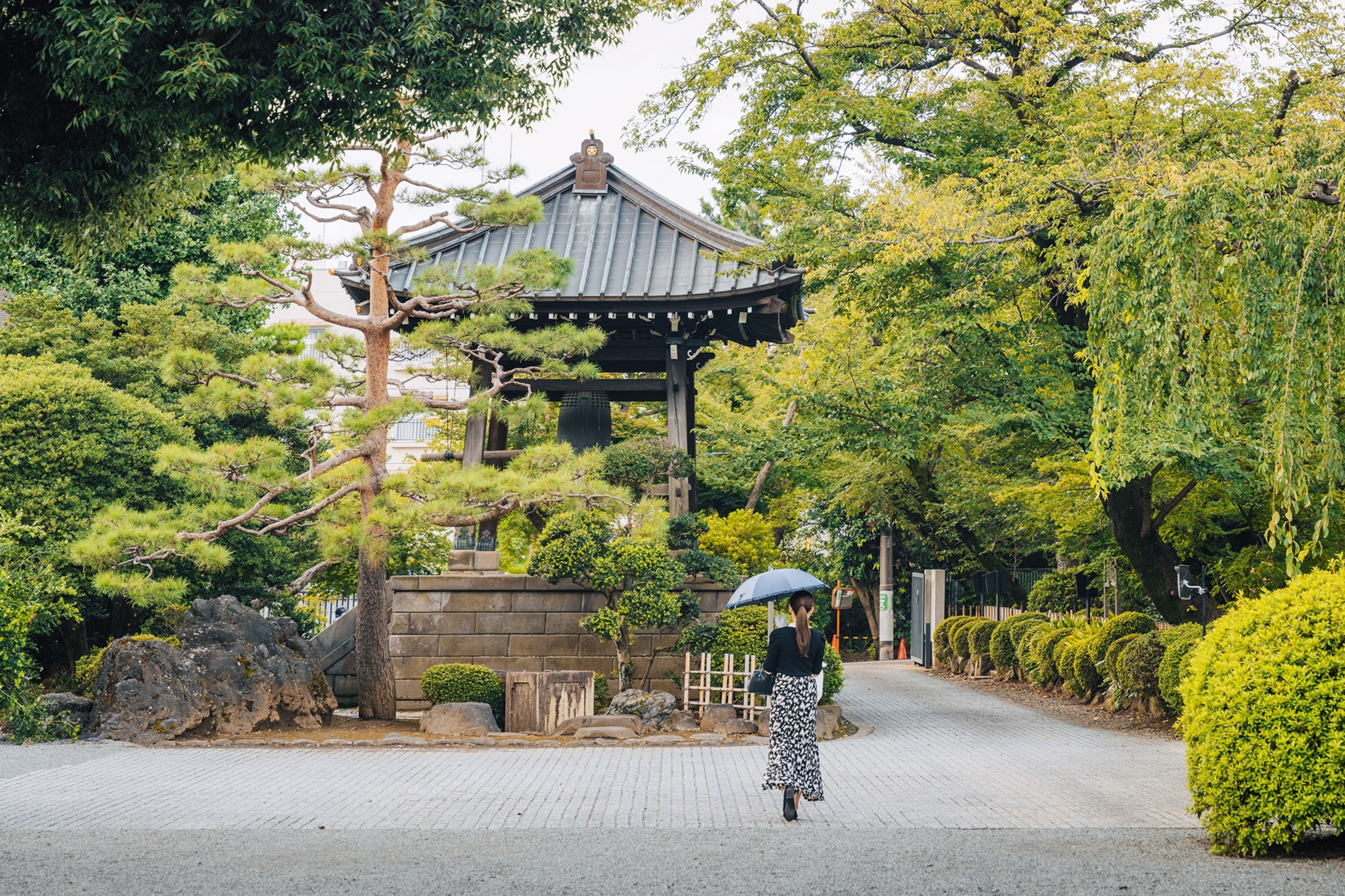 Gotokuji temple near Tokyo, surrounded by many trees and bushes. A woman is walking towards the temple to enter.