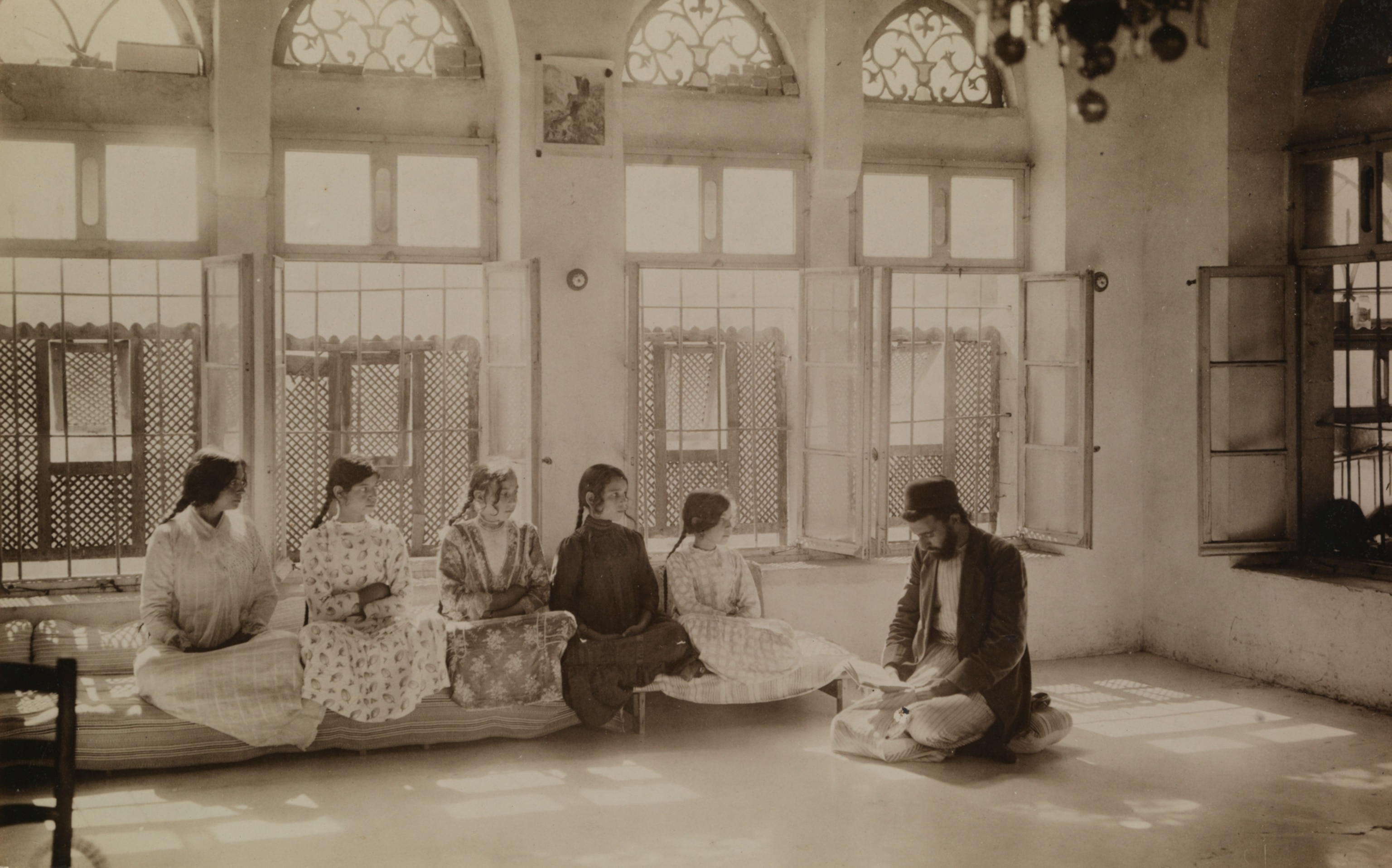 Samaritan girls sit beside one another as they listen to their teacher, who is kneeling on the floor