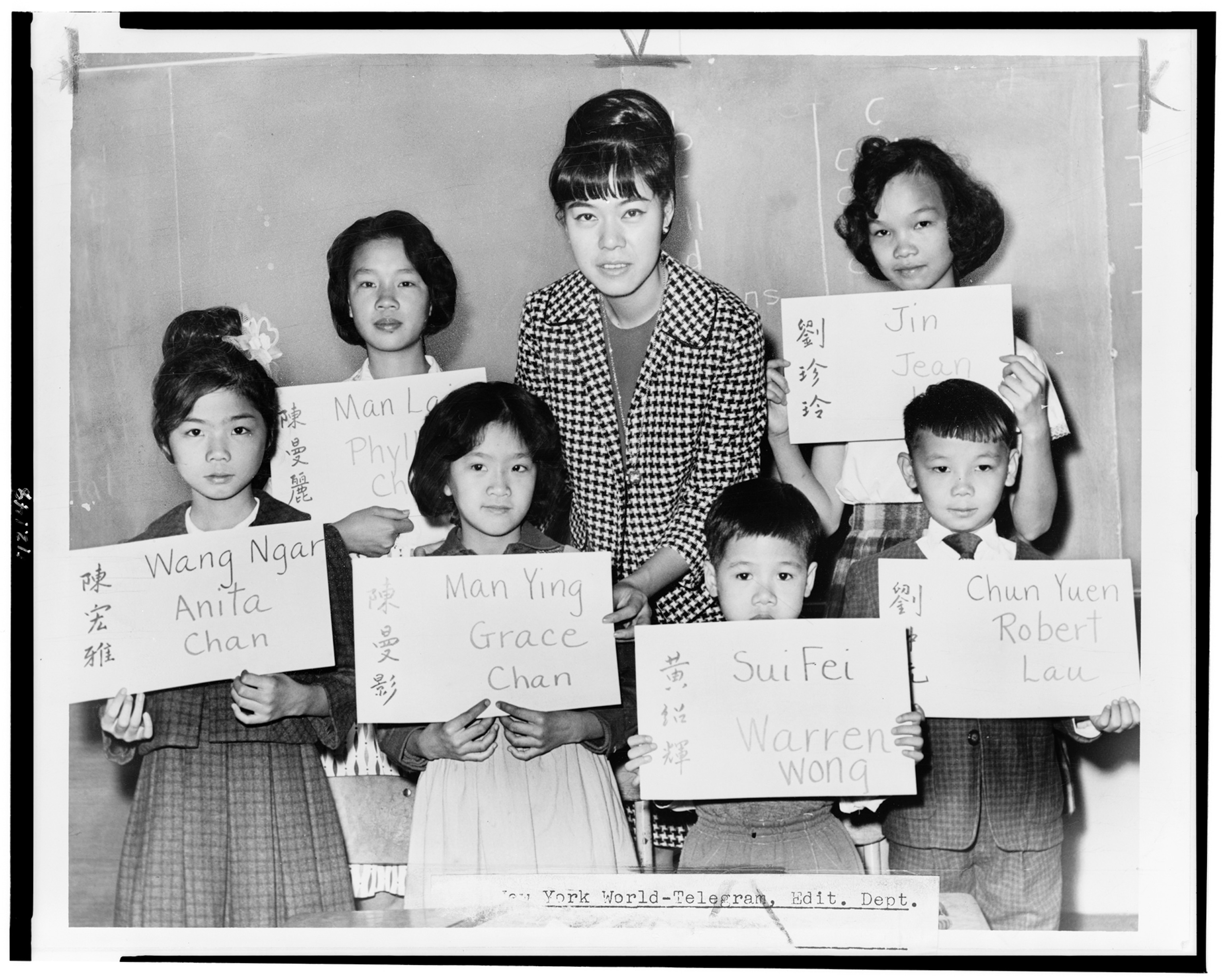 A school teacher poses with a classroom of children holding up signs of their names spelled in English and Chinese