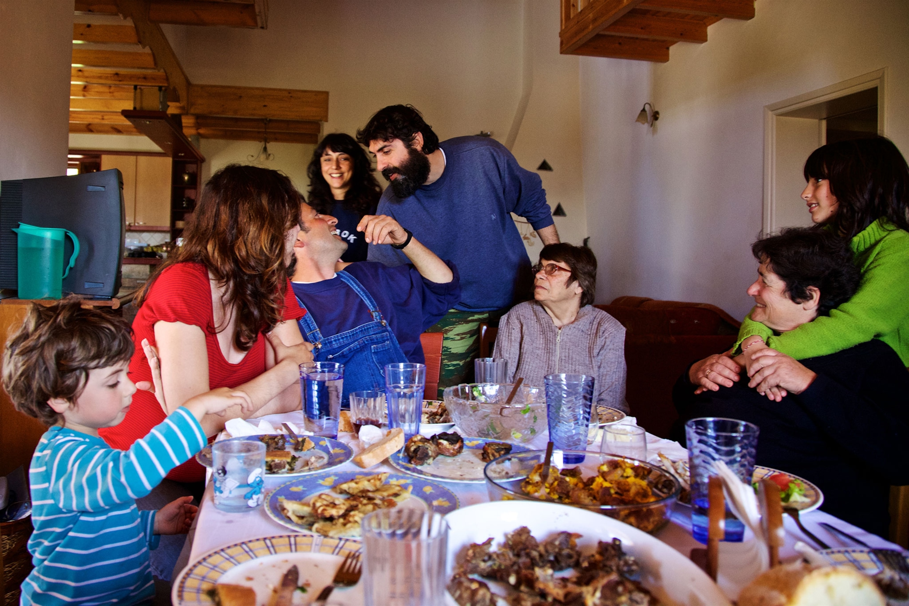 A family gathers around a table with food and drinks inside a home.