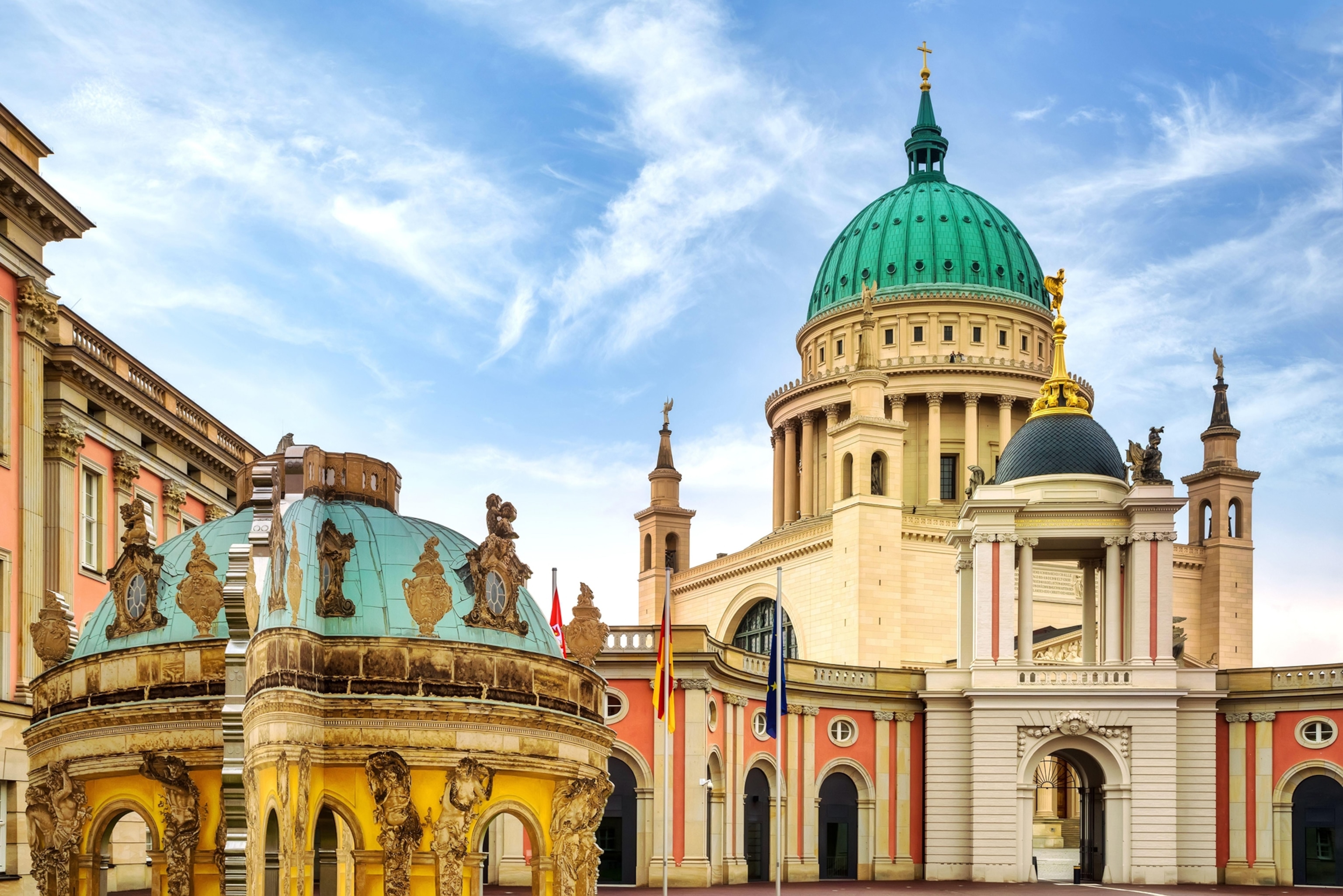 Two buildings in front of a slightly cloudy blue sky. The buildings both have dome ceilings.