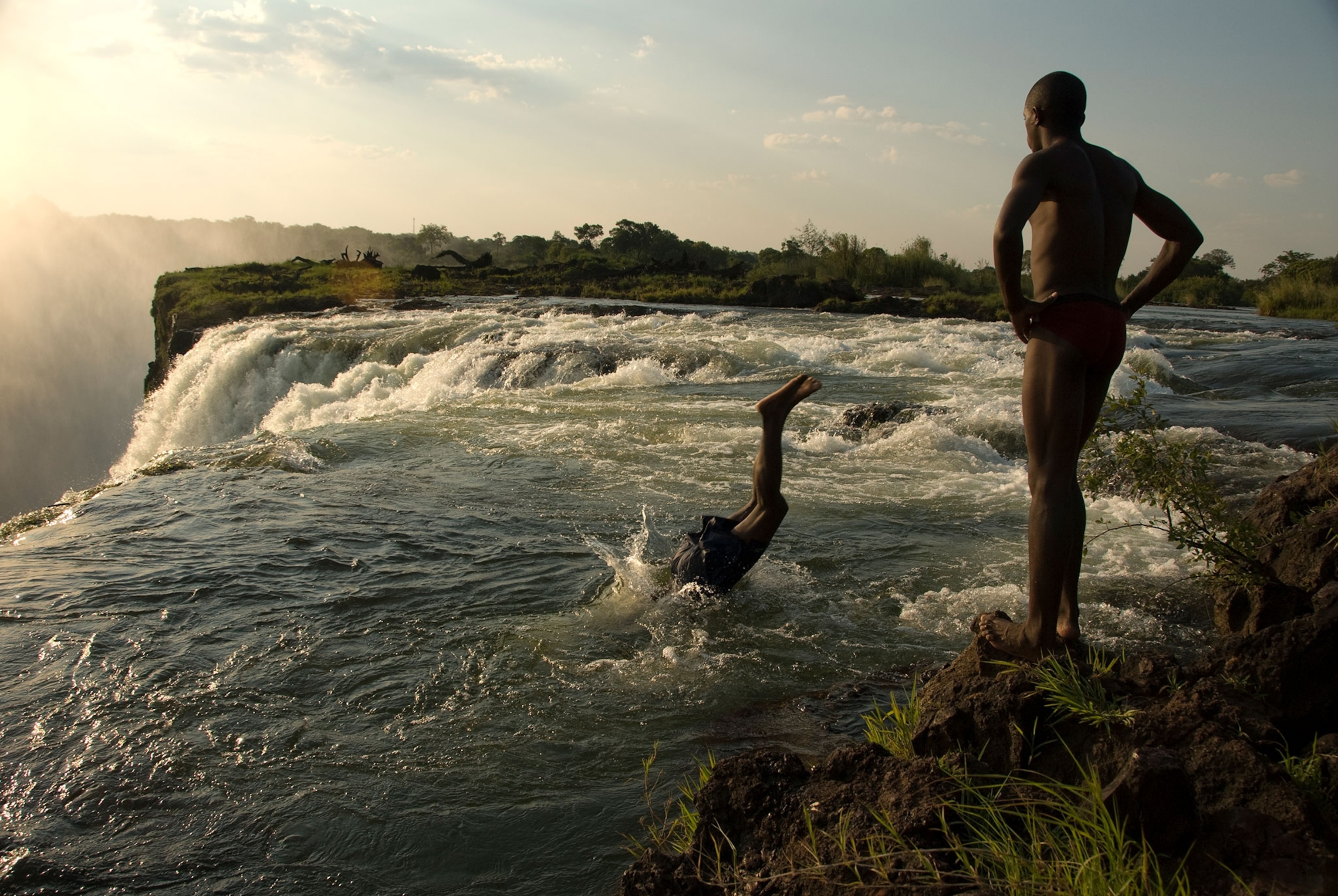 people diving into a pool at the edge of victoria falls