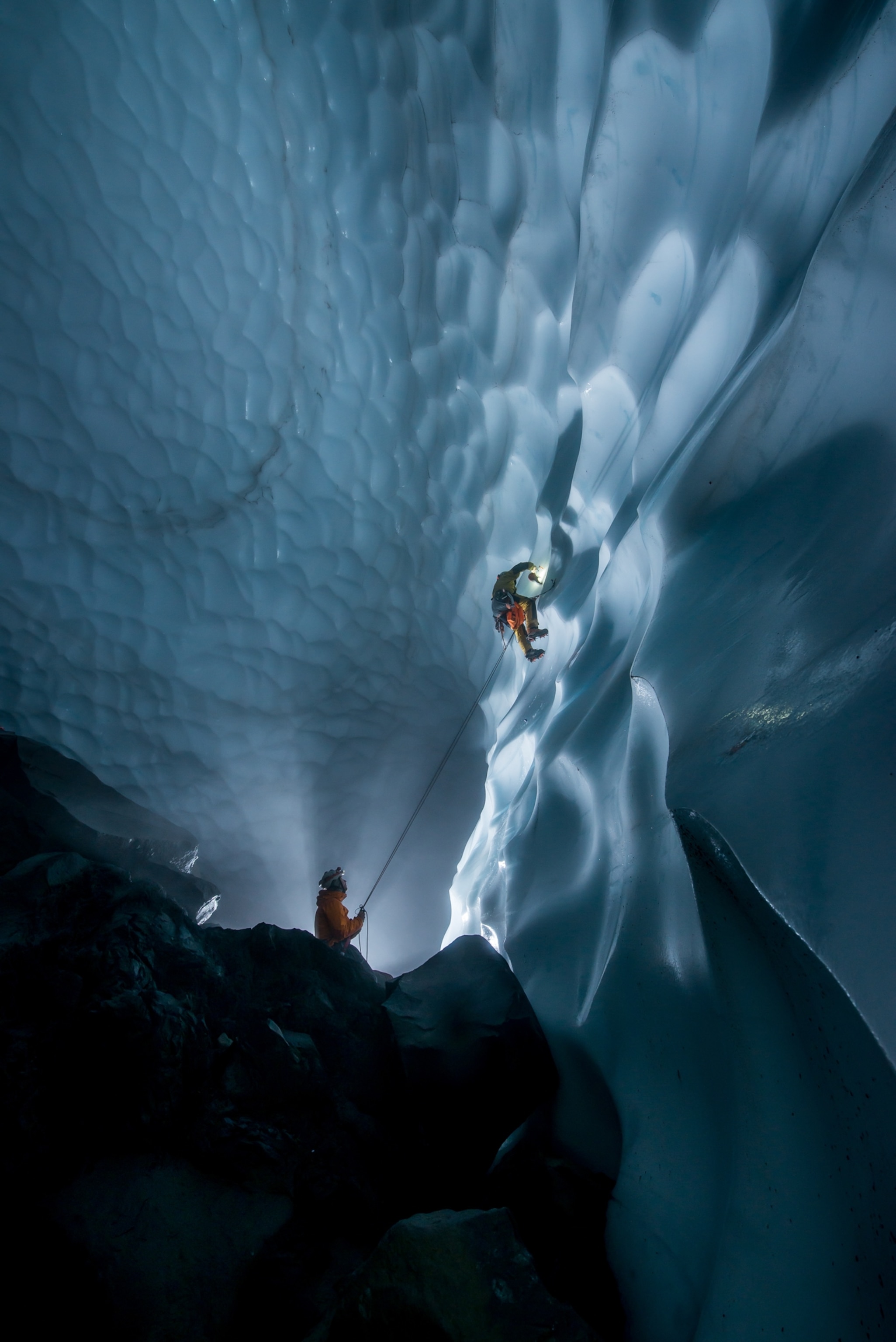 Expedition members using belay gear to climb a wall of ice in the ice cave.
