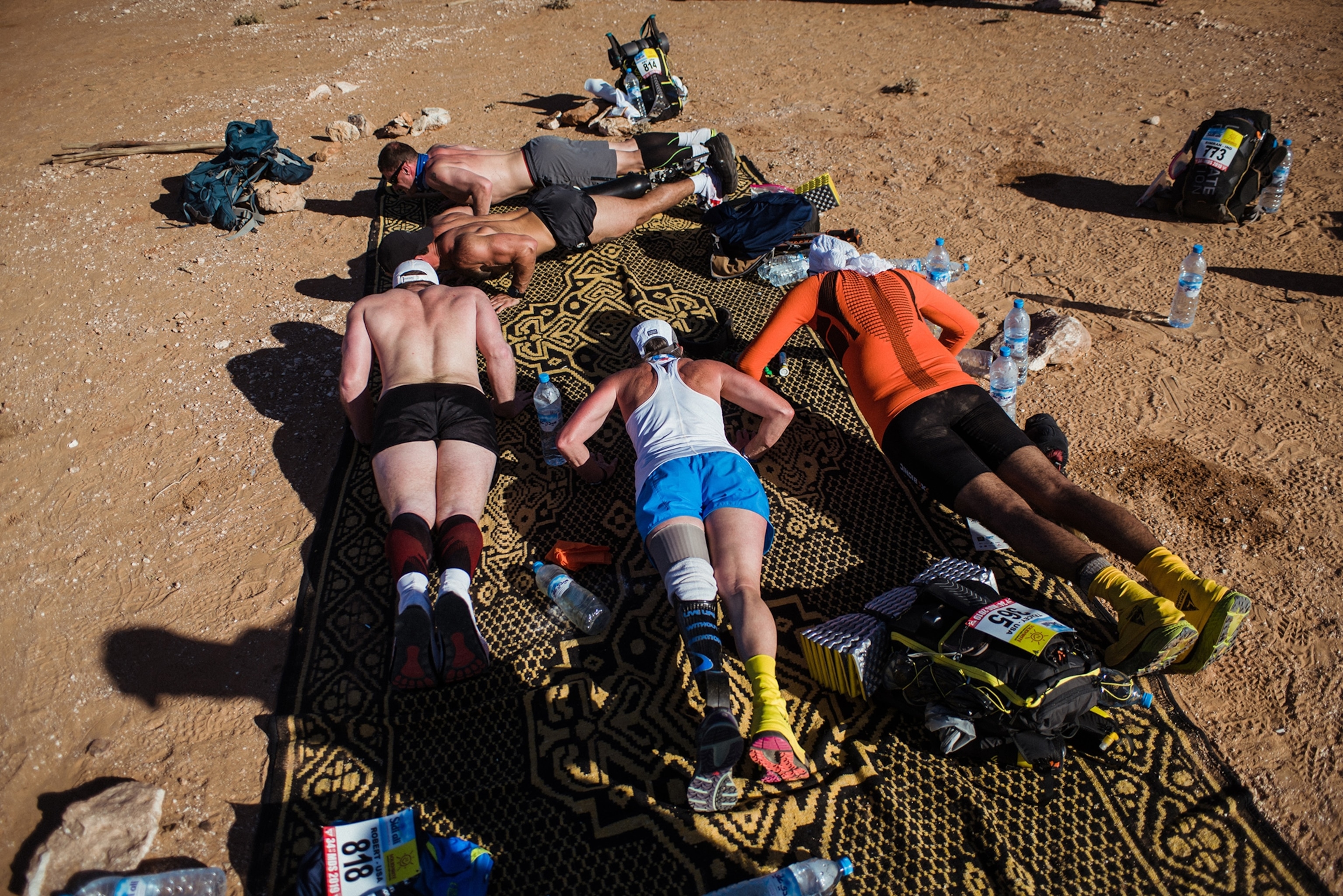 A group of athletes do push-ups in the sand.