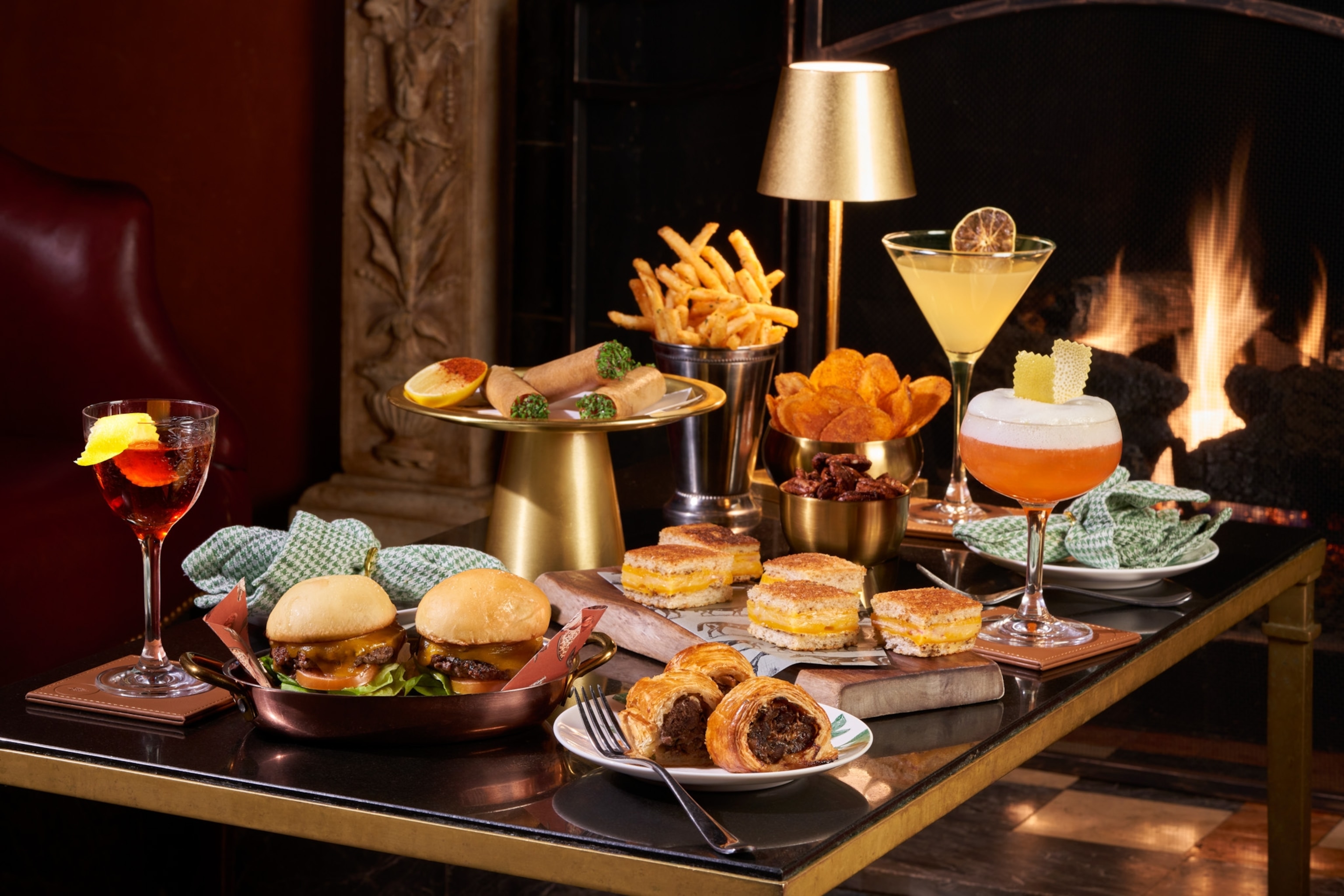 A table full of food and cocktails sitting in front of a fireplace.