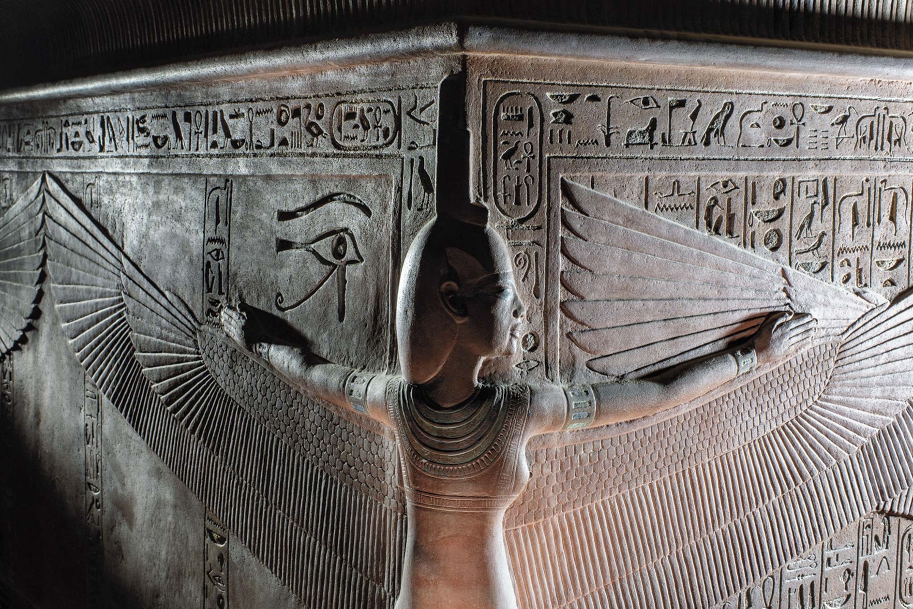 A stone carving of an ancient Egyptian god with wings surrounded by heiroglyphics