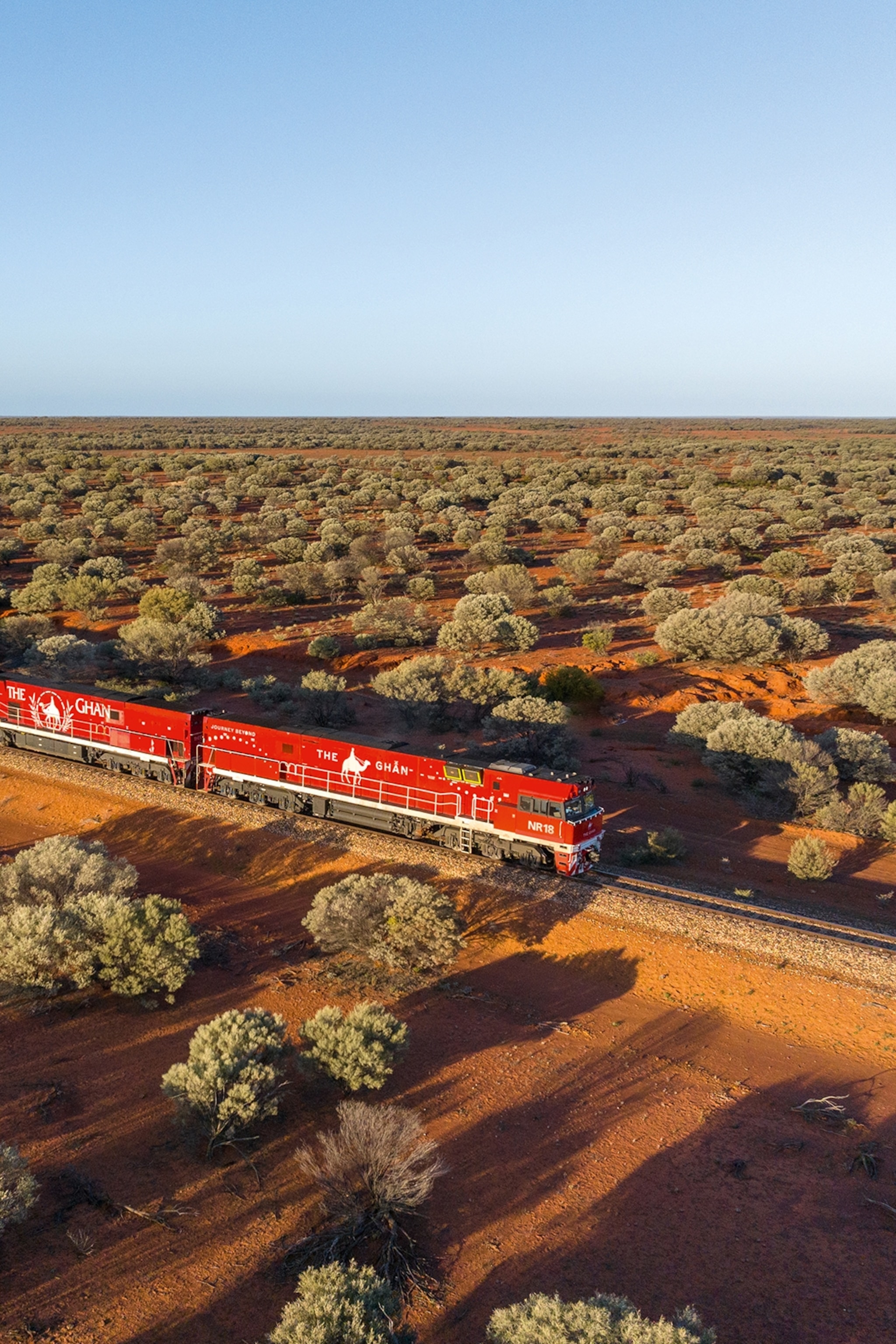 A train passing through a desolate, flat and bushy landscape at dusk.