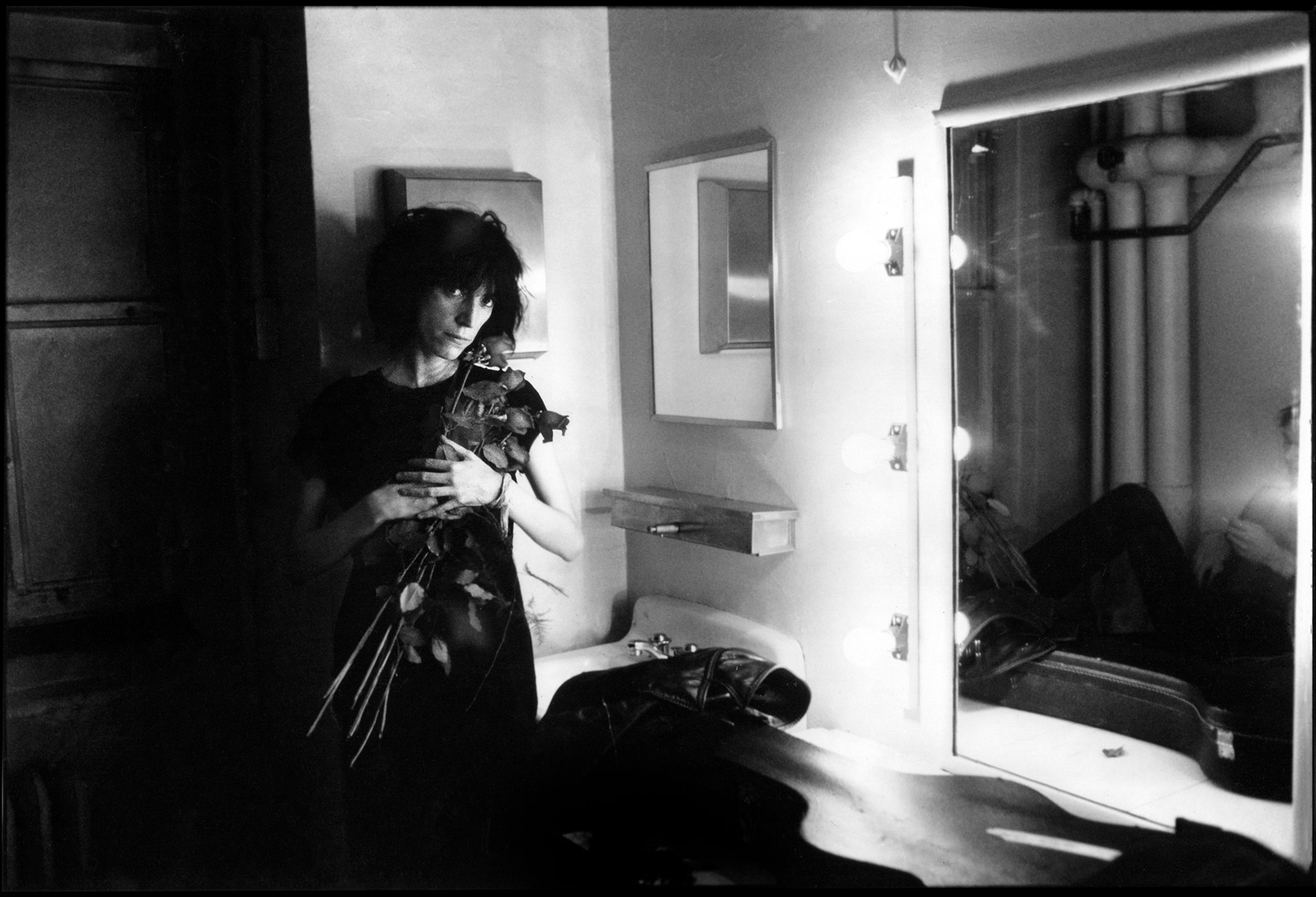 A black and white photo of a woman holding roses in a dressing room backstage of a performance center