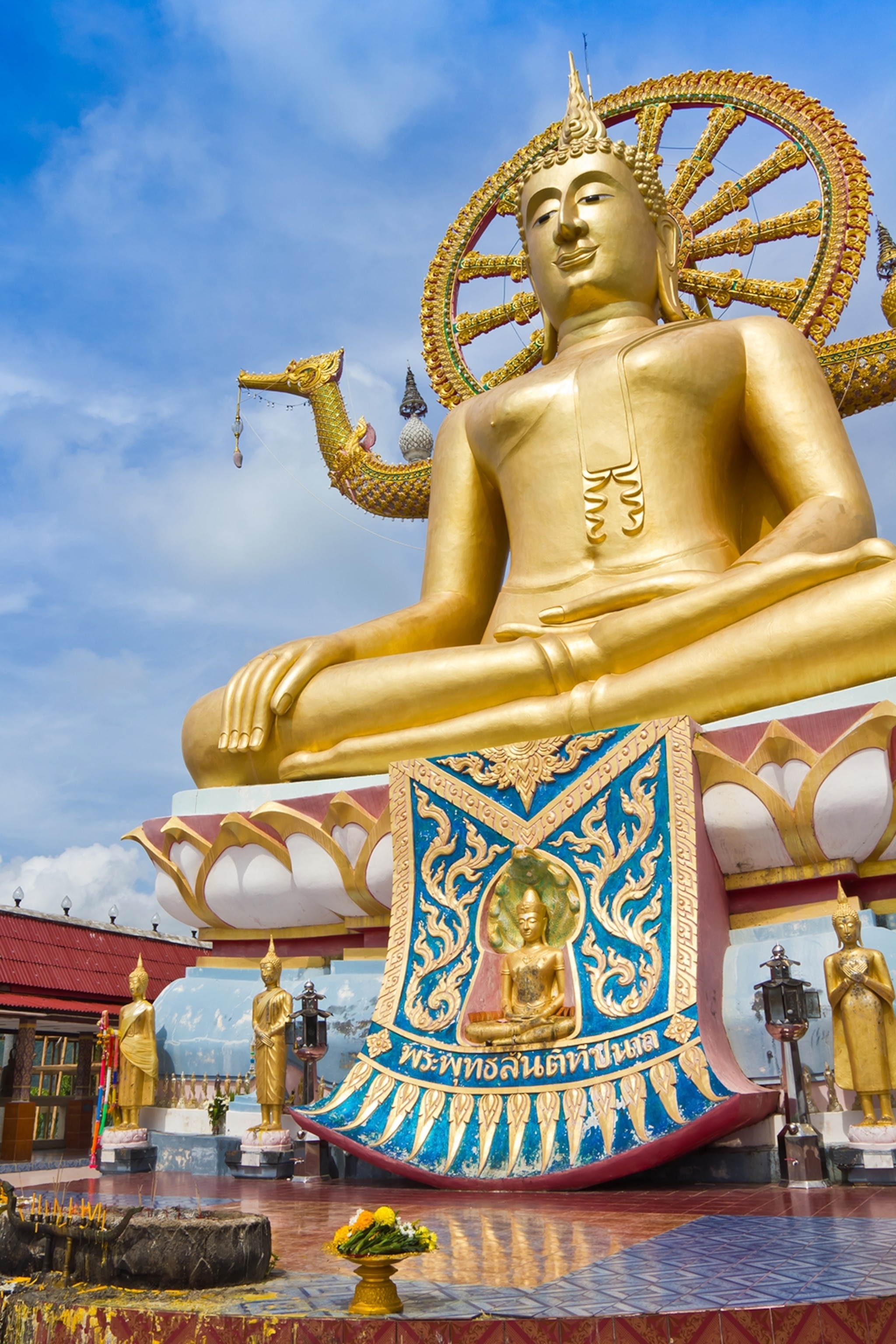 A massive golden Buddha statue in a seated position against clear skies, raising one hand.