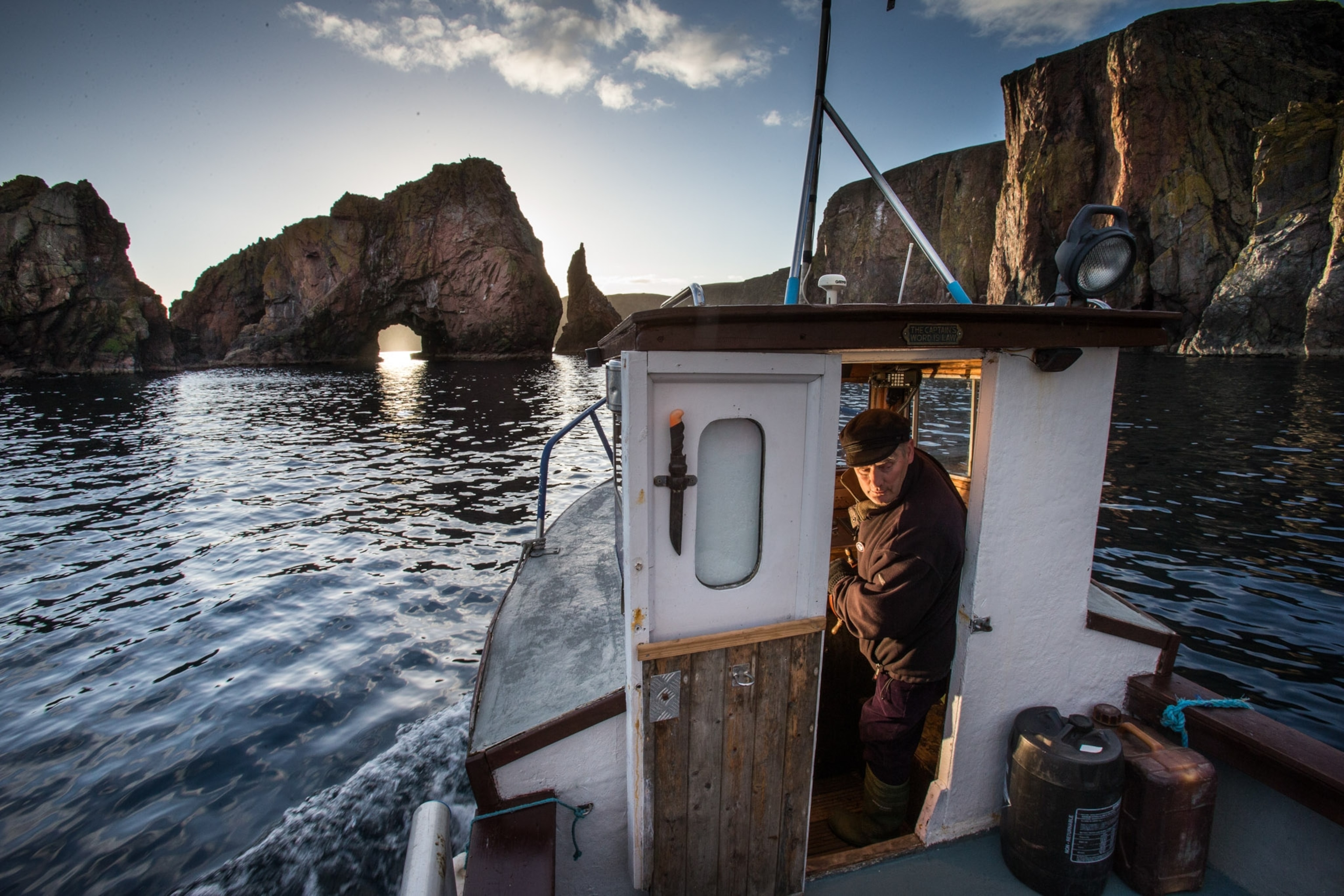 A man with grey hair looks out the door of his small boat, calm waters and beautiful sky.