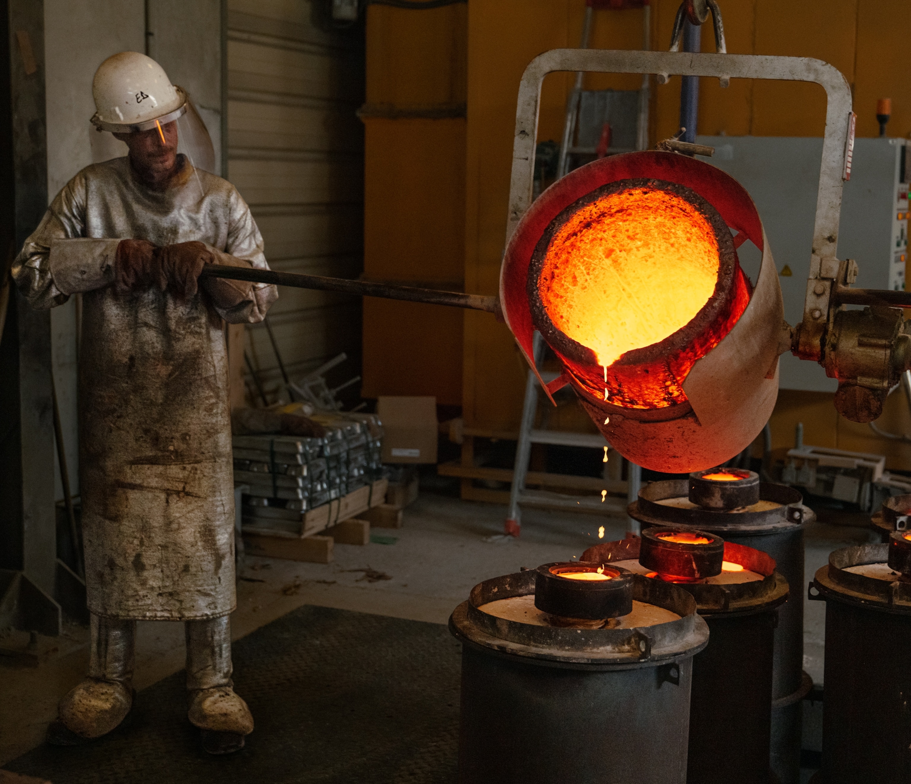 A worker wearing special gear pours molten bronze into a mold