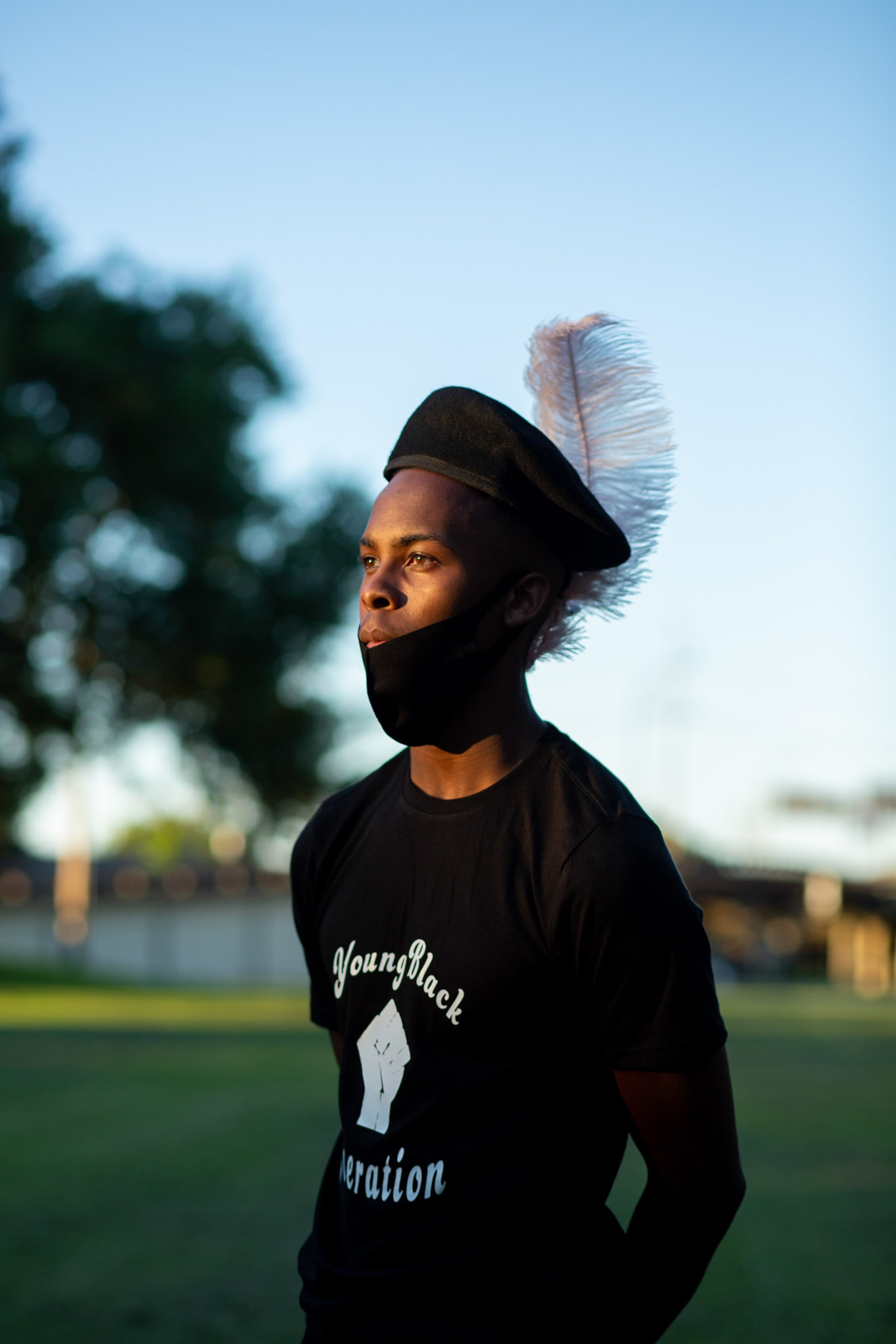 young man standing at sunset wearing a hat with a feather on the back