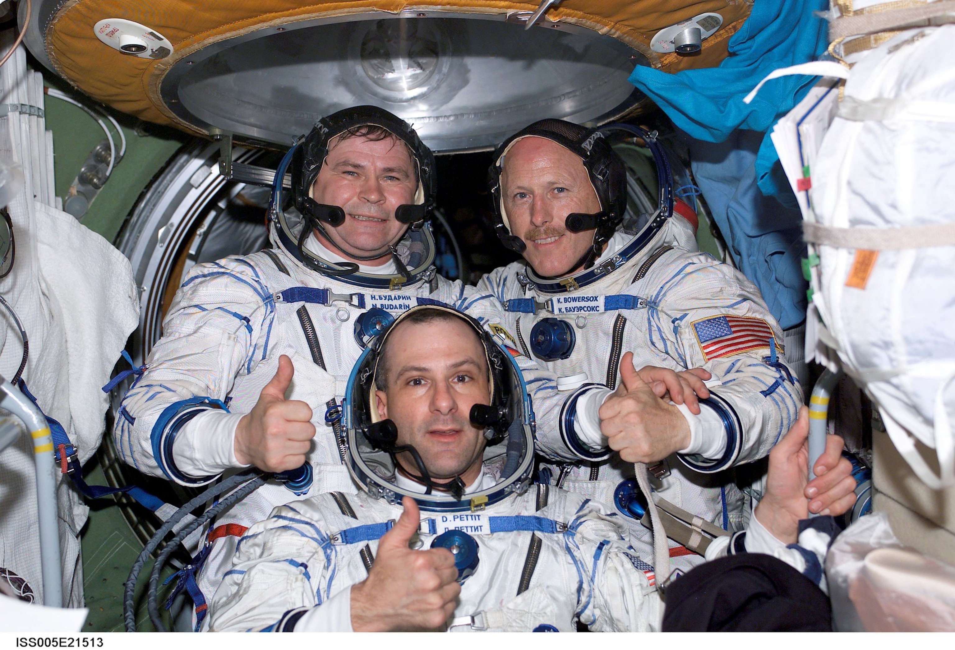 Three men in white space suits with thumbs up inside Space Station