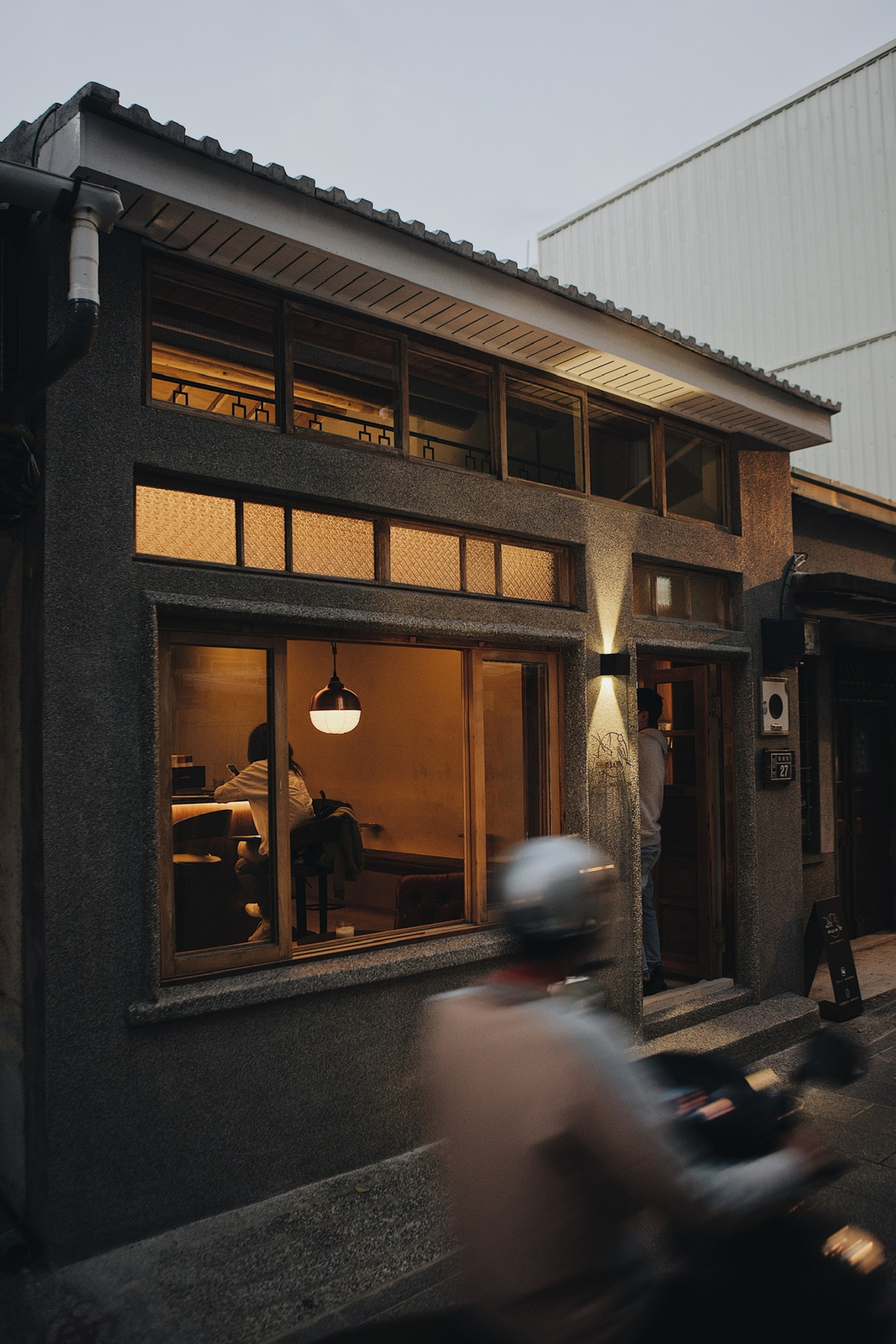 Exterior of a coffee shop and bar with people passing by on a cloudy day.