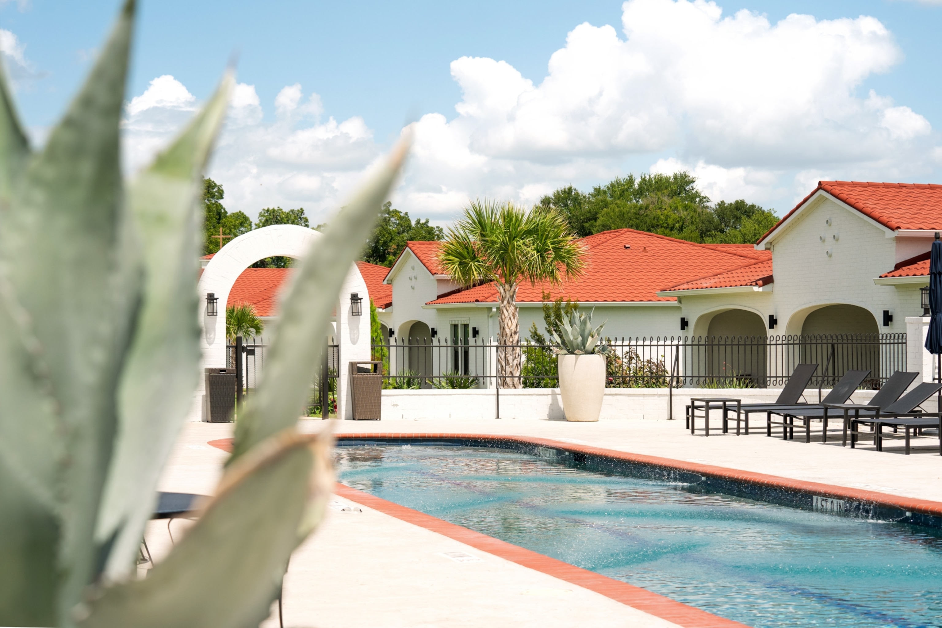 A blue pool sits in front of white buildings with orange roofs.