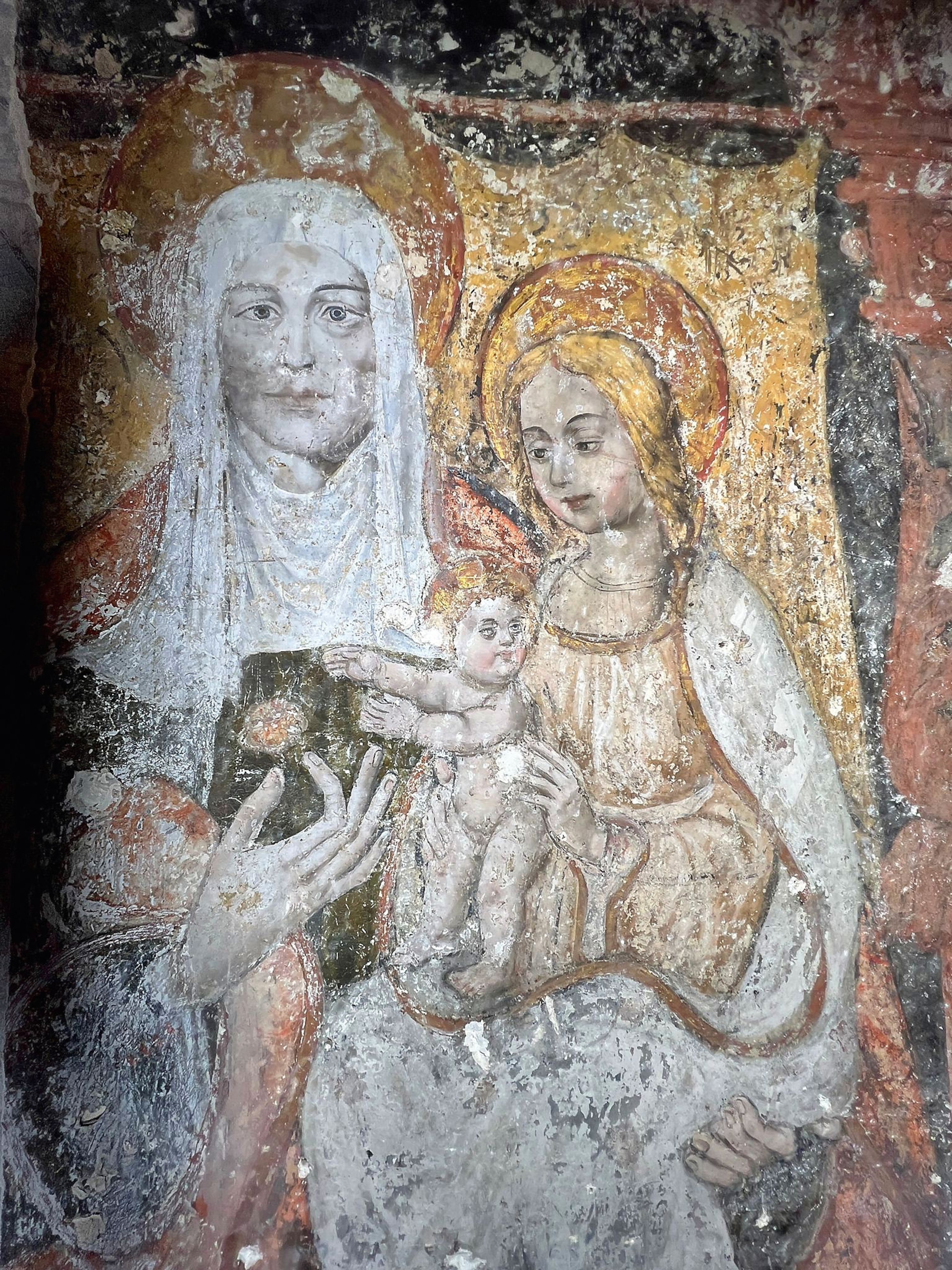 A worn fresco of a woman holding a child who is holding a baby