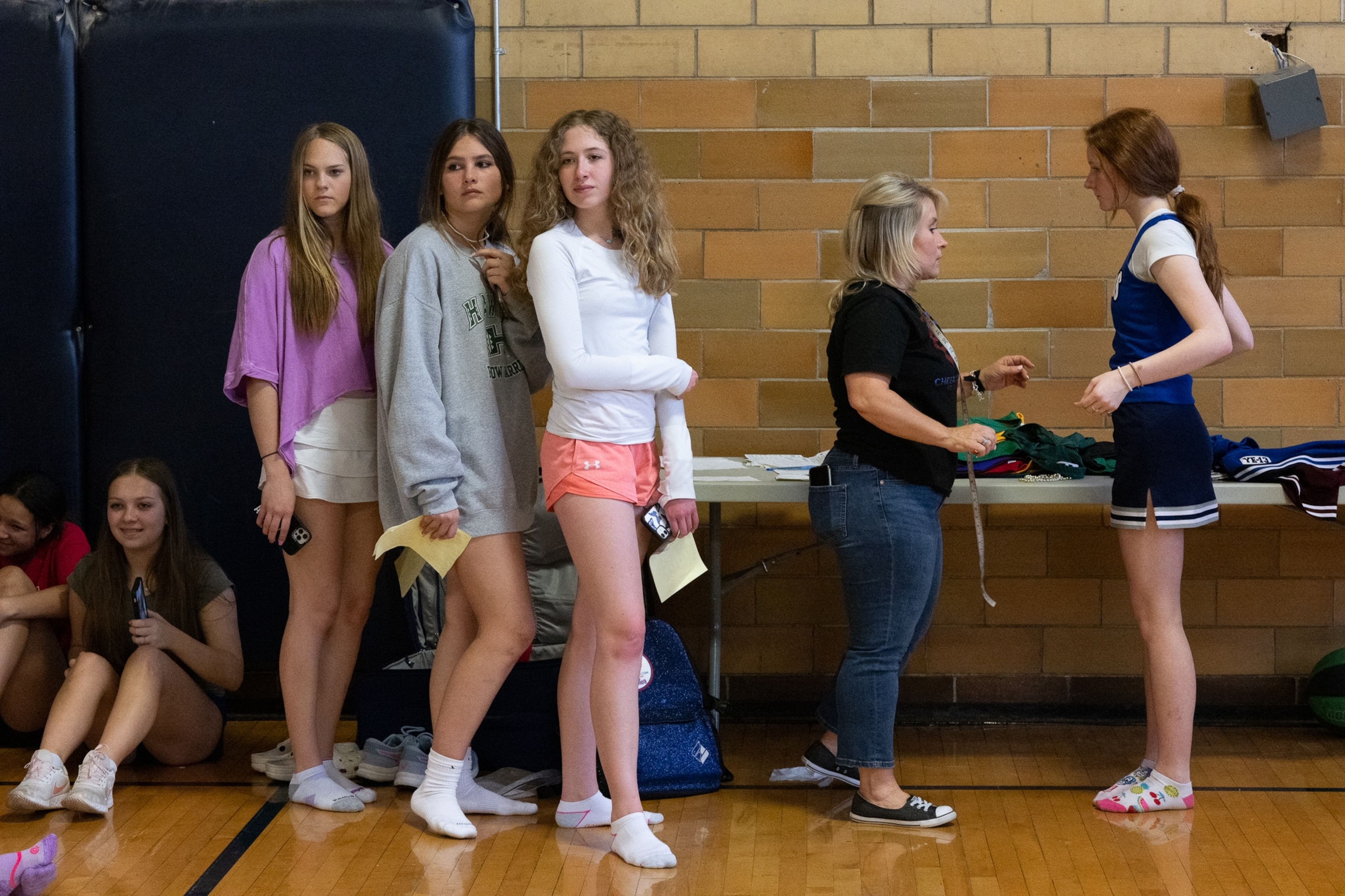 female students stand in line inside a gymnasium waiting to get fitted