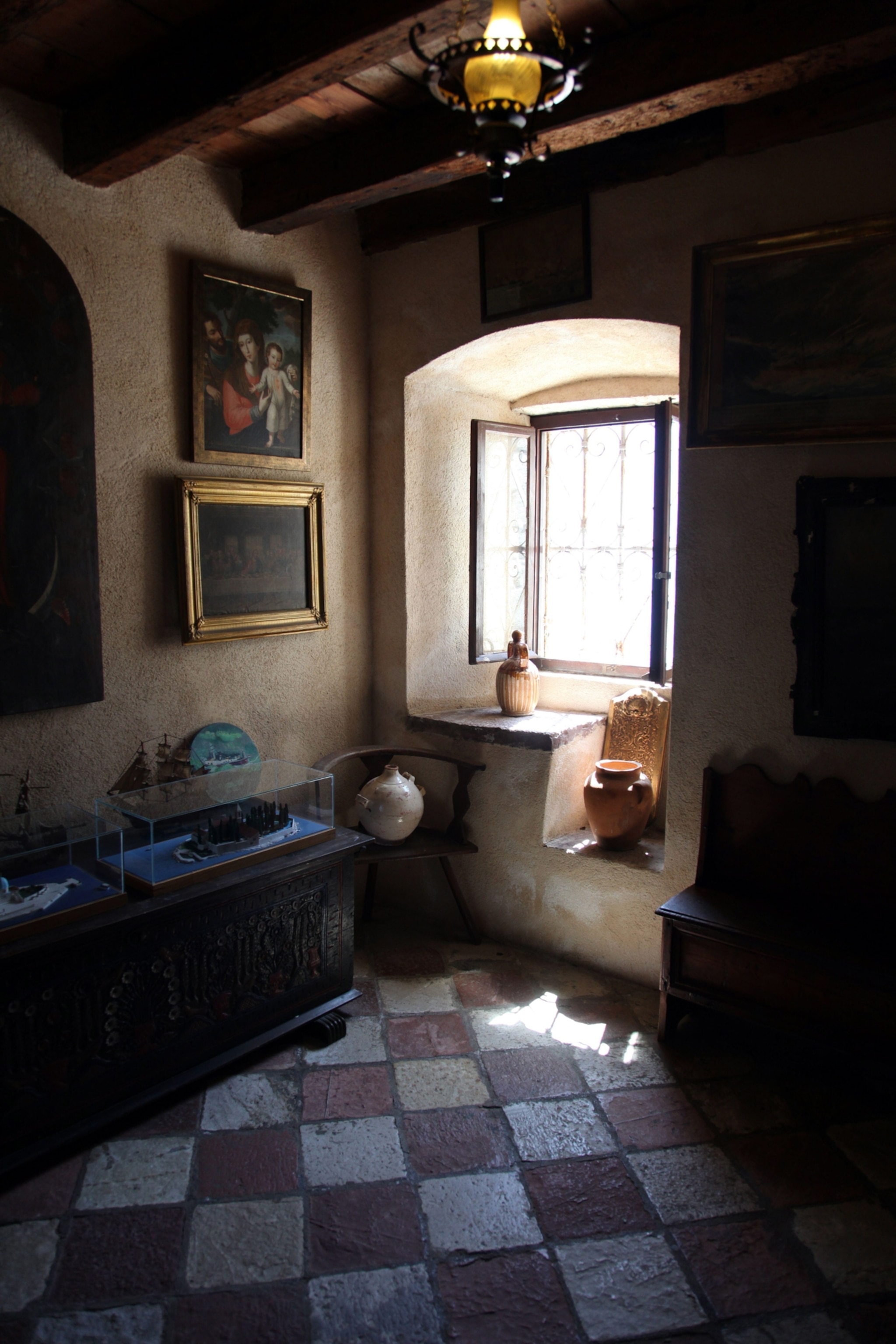 Light passes through a window at the Sacristy of Church of Our Lady of the Rock; the room is adorned with paintings and decorative vases.