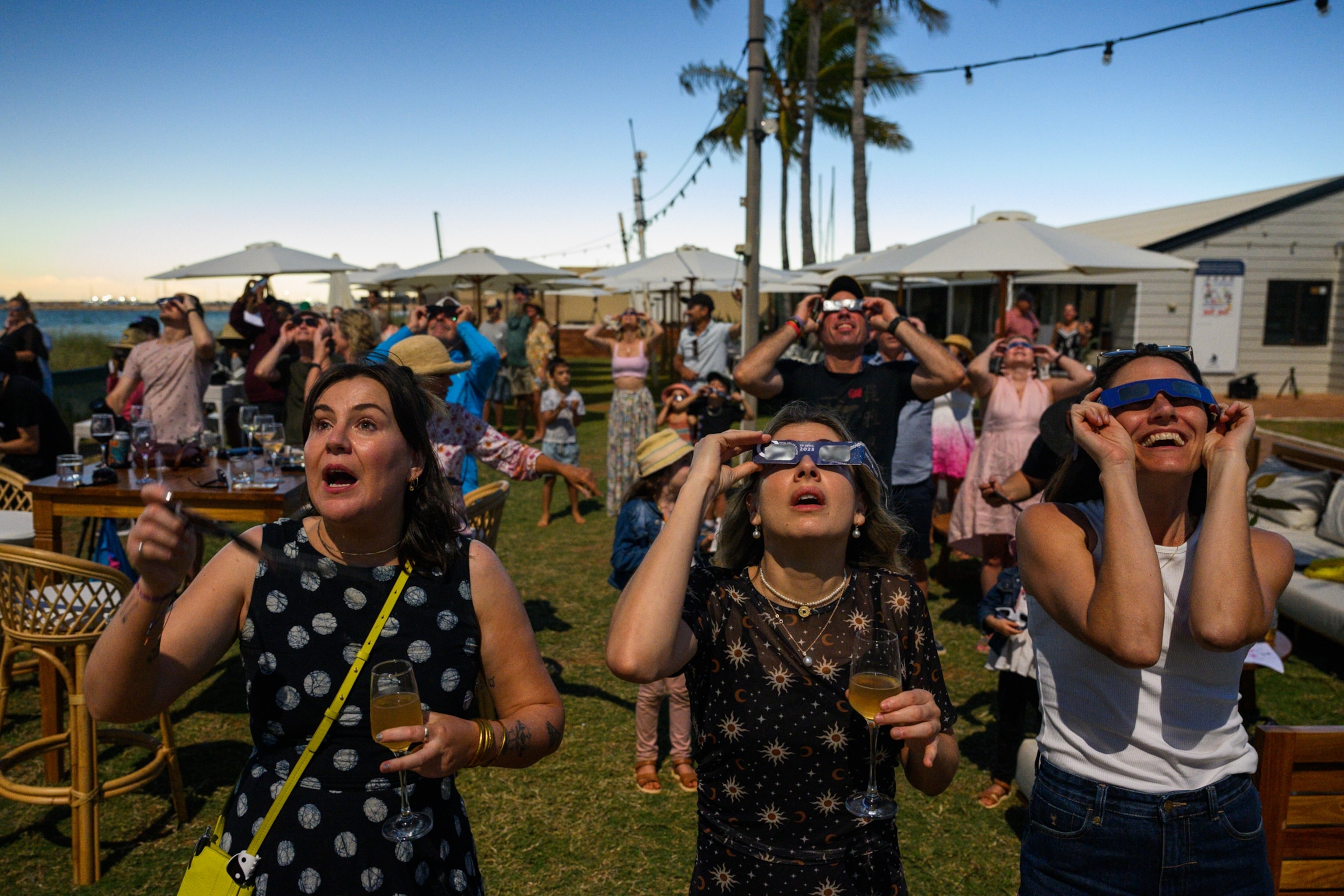 A crowd of onlookers watch a total solar eclipse with looks of surprise, glee, and surprise.