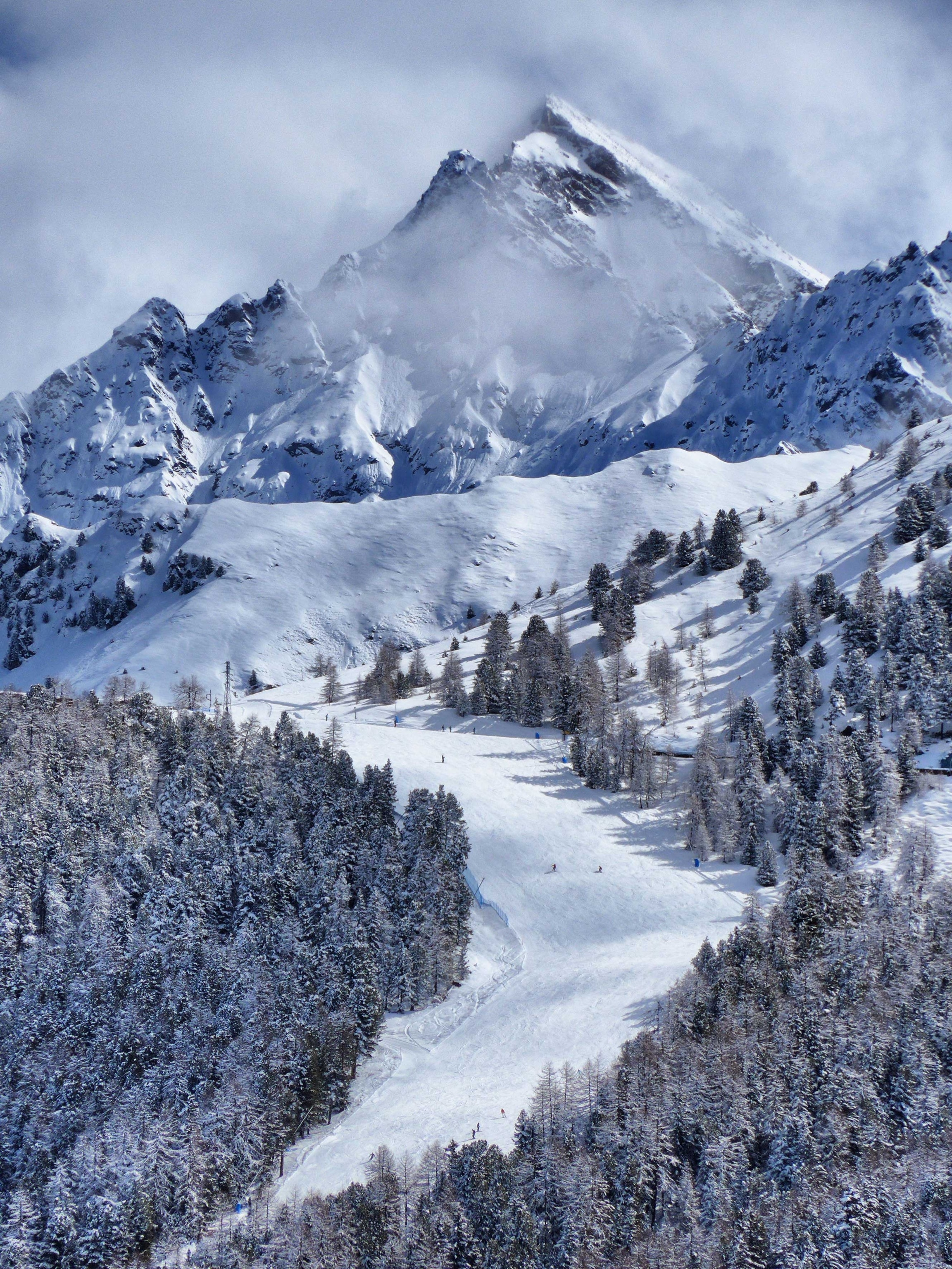 A wide, well-groomed ski slope, with a background of snow-covered peaks.