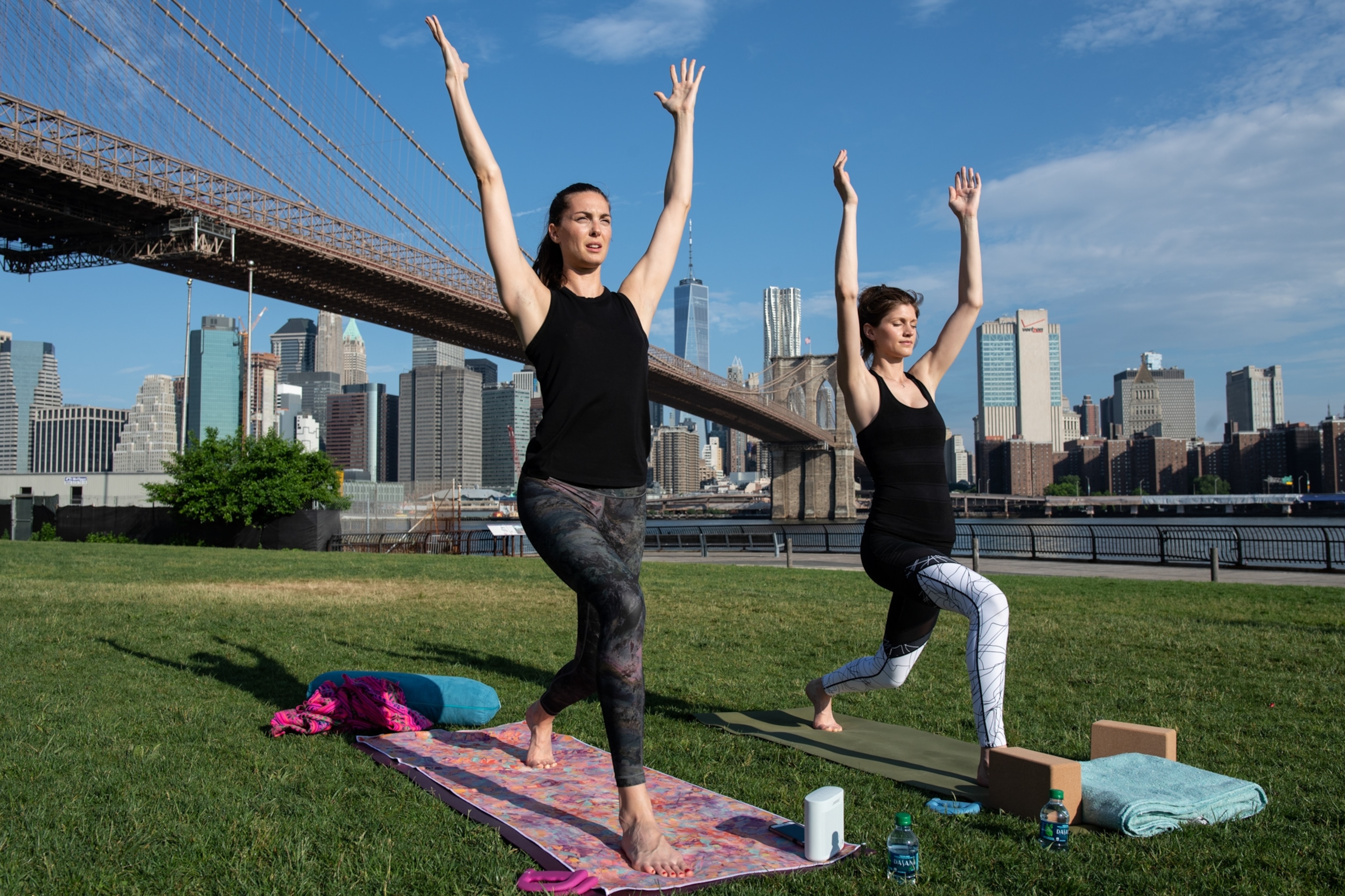 Two women with their arms outstretched as they practice yoga near Brooklyn Bridge.