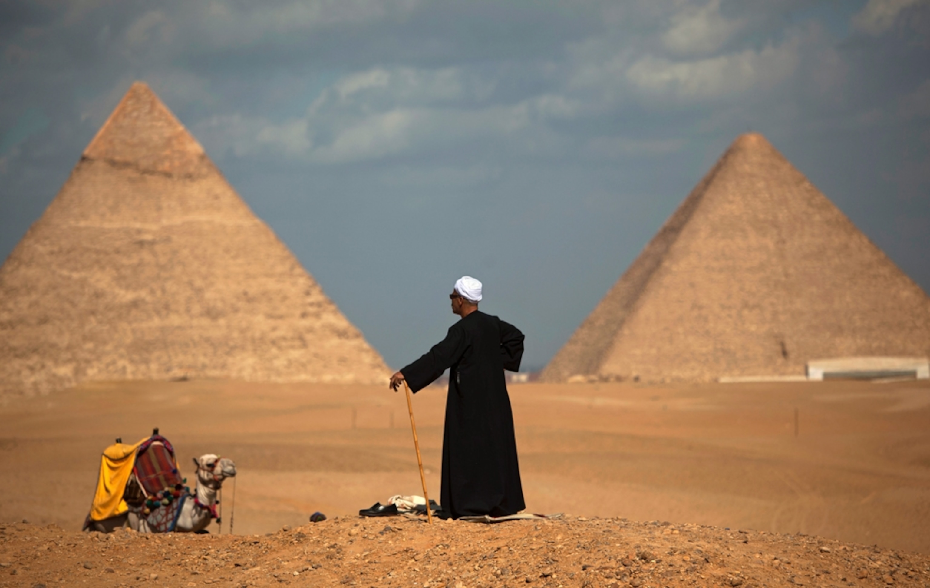 Man stands on a desert hill with Giza pyramids in the background