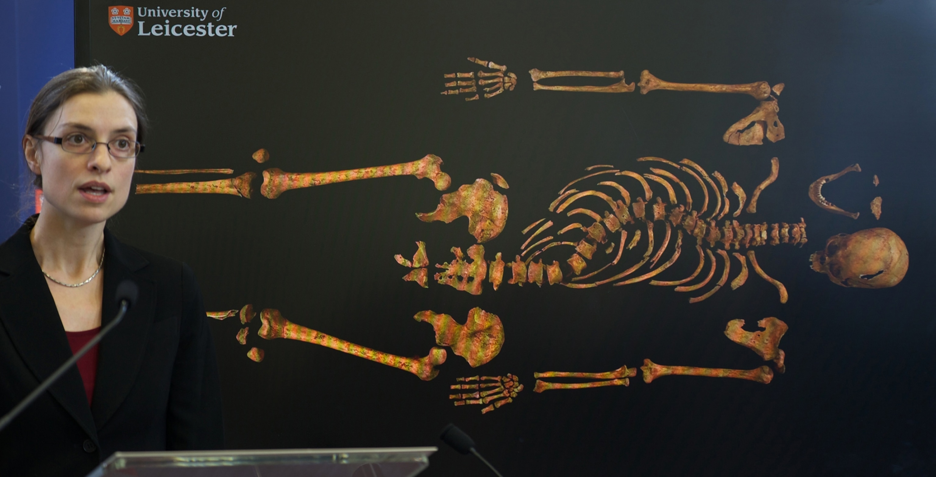 Photo of woman at lectern with photograph of skeleton on screen behind her