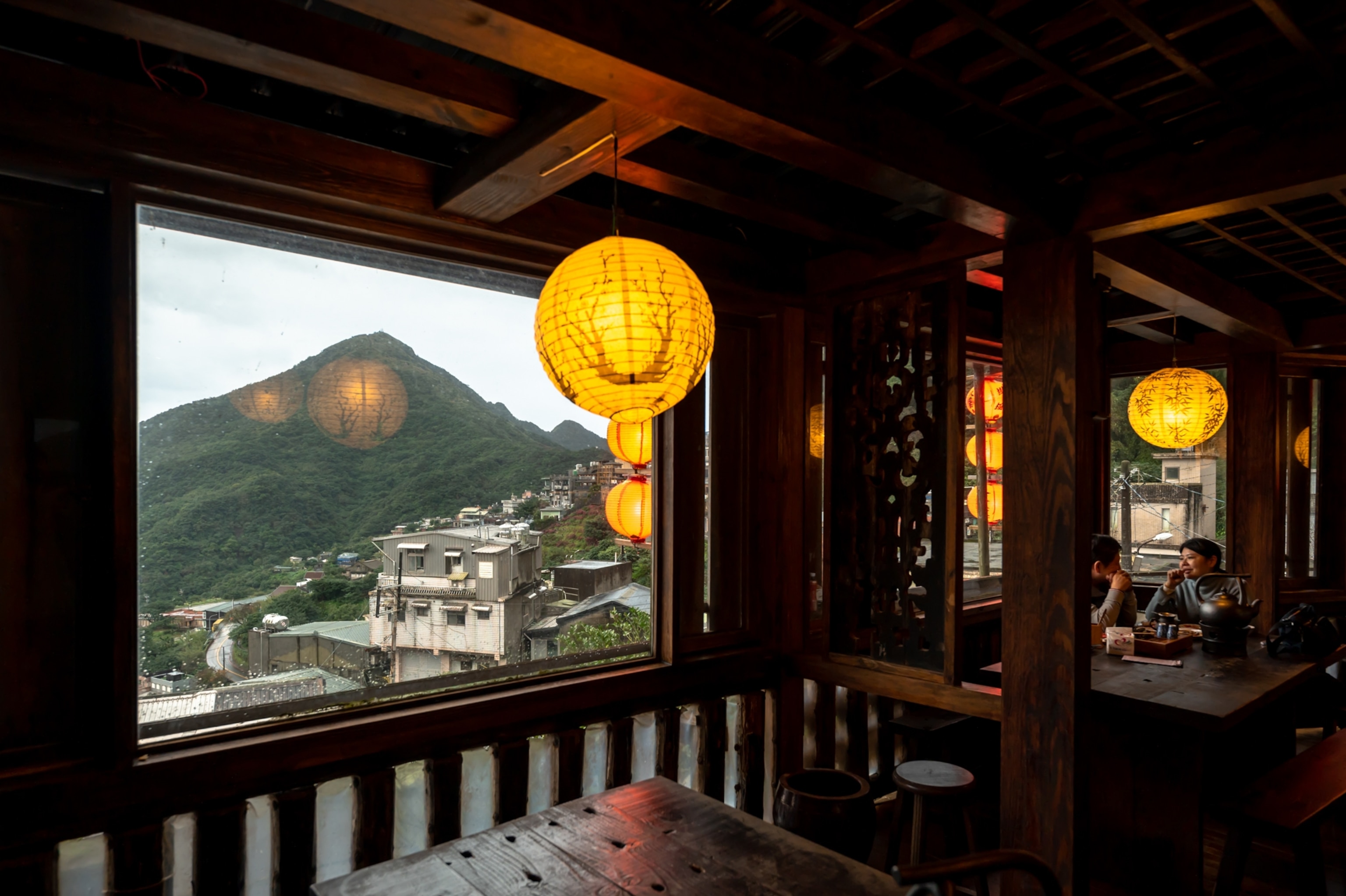 Visitors drink tea in Jiufen's Shu-ku Tea House nested within Taiwan's northern seaside mountain ranges seen through a window