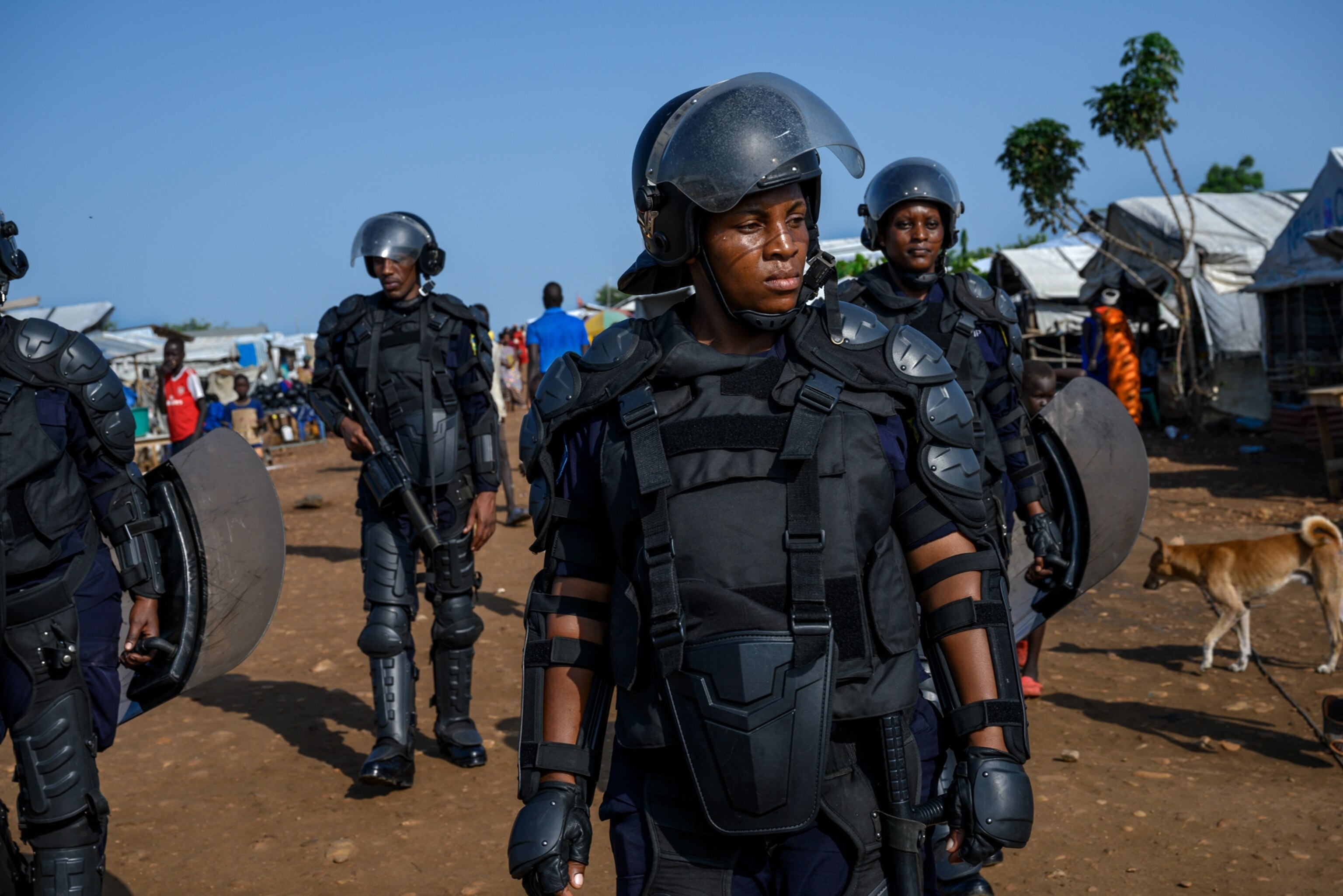 a woman covered in armed gear, standing in front of a civilian camp