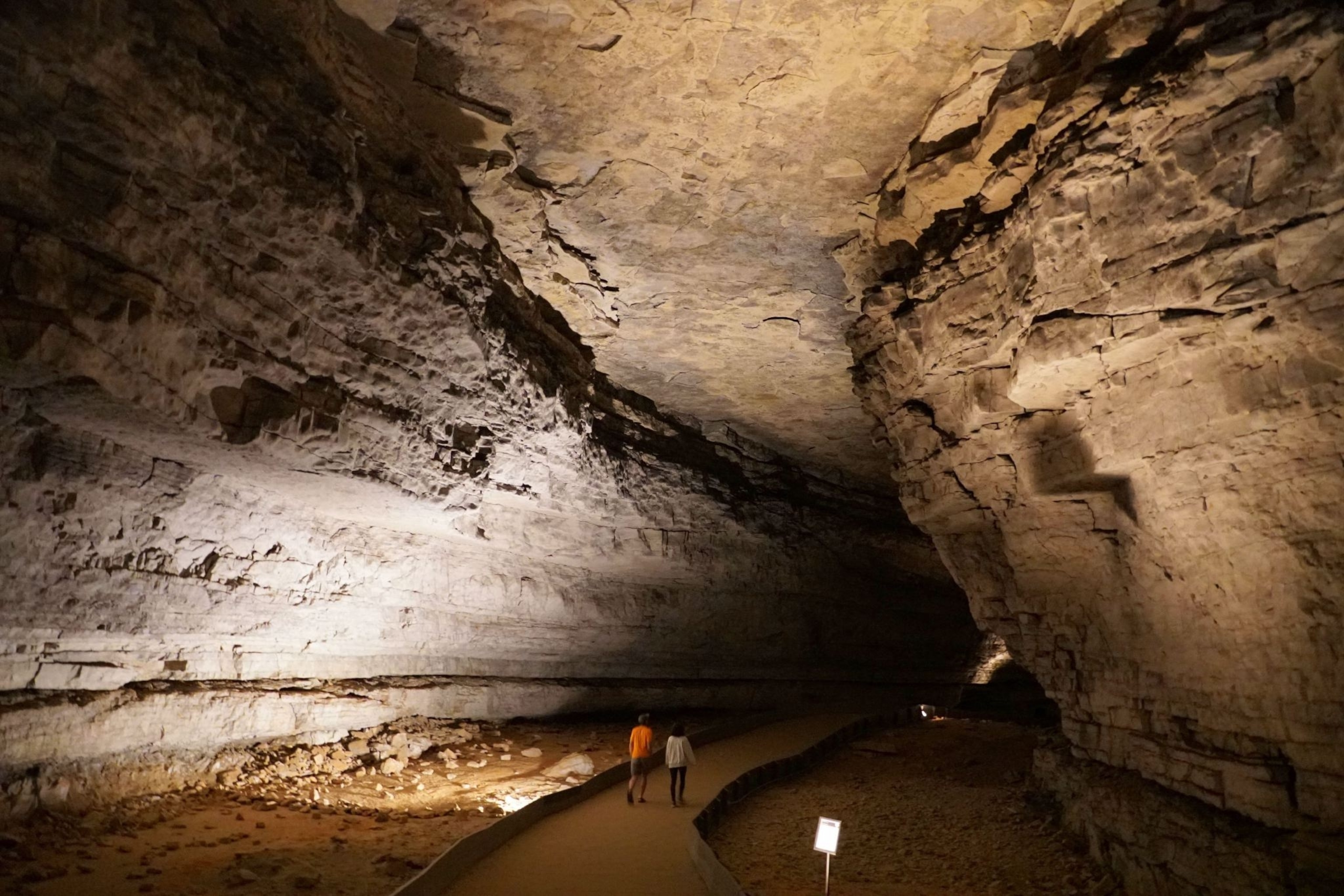 A pair of people walk along a path that cuts through a huge opening within the Mammoth cave system