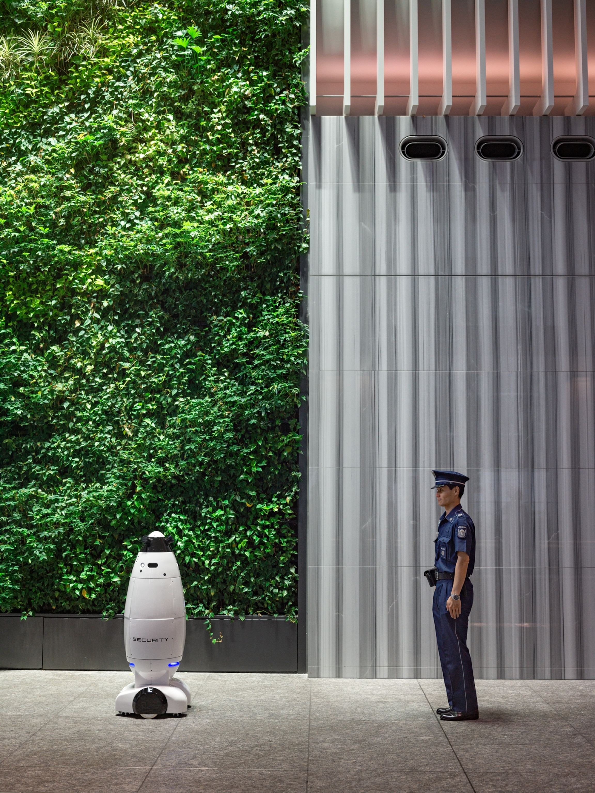 cylindrical white robot next to security guard.