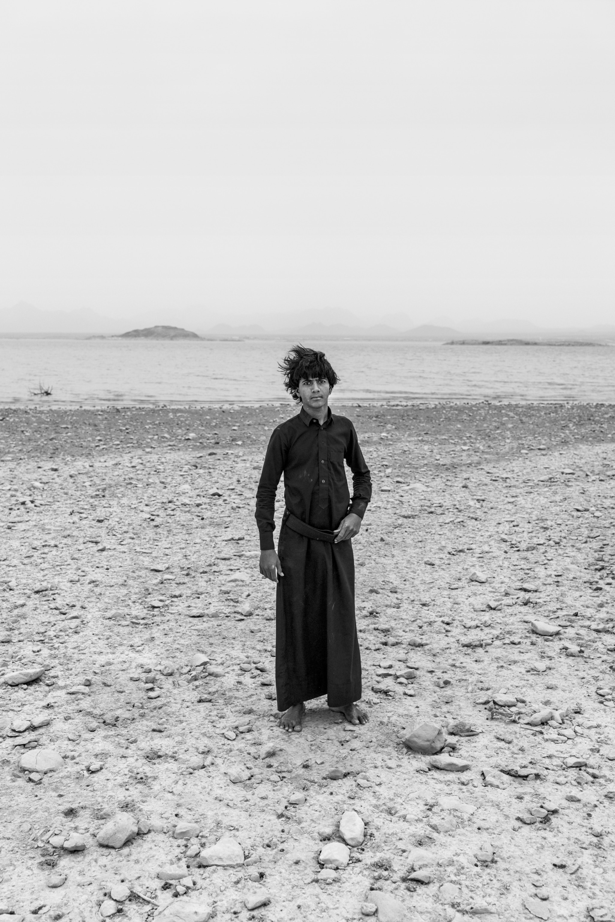 Picture of bearfoot young man in black dress near body of water.