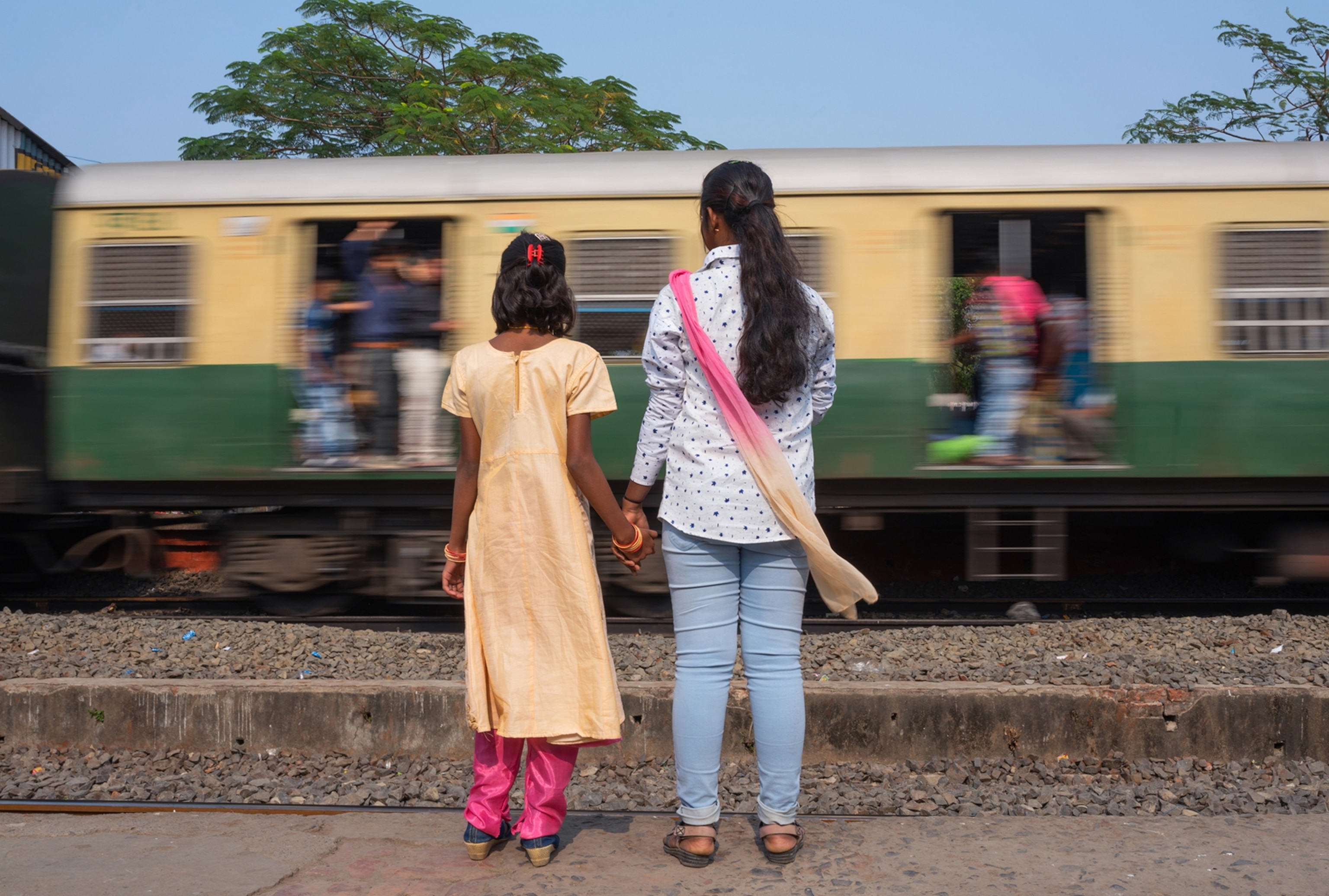 one young woman and one girl standing hand in and looking at a passing train