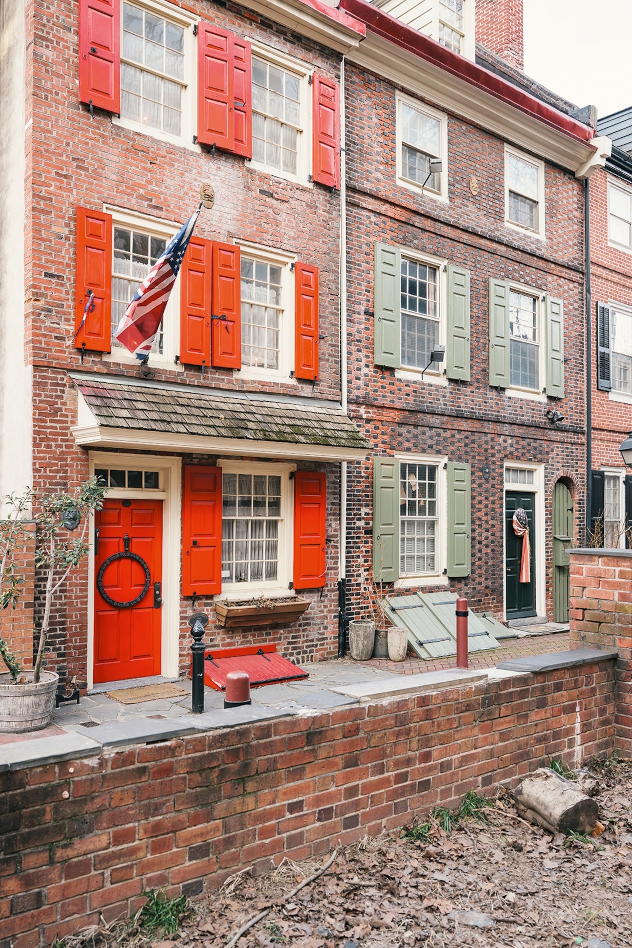 An old cobblestone street with a red brick house with red doors, and red window shutters.