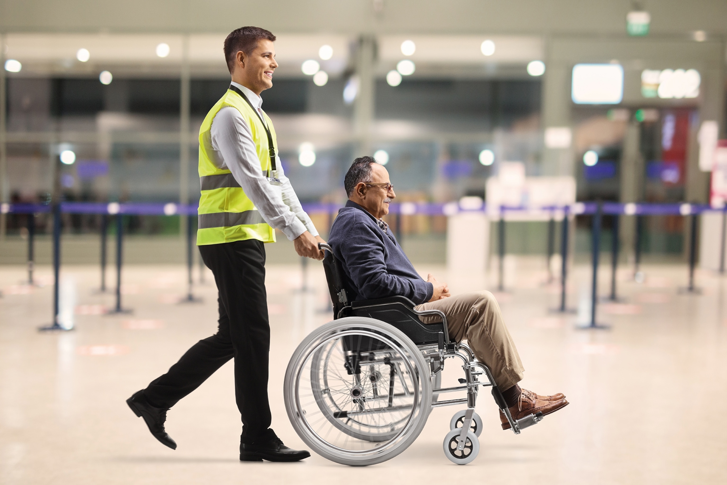 An elderly man in a wheelchair being pushed by a member of airport staff.