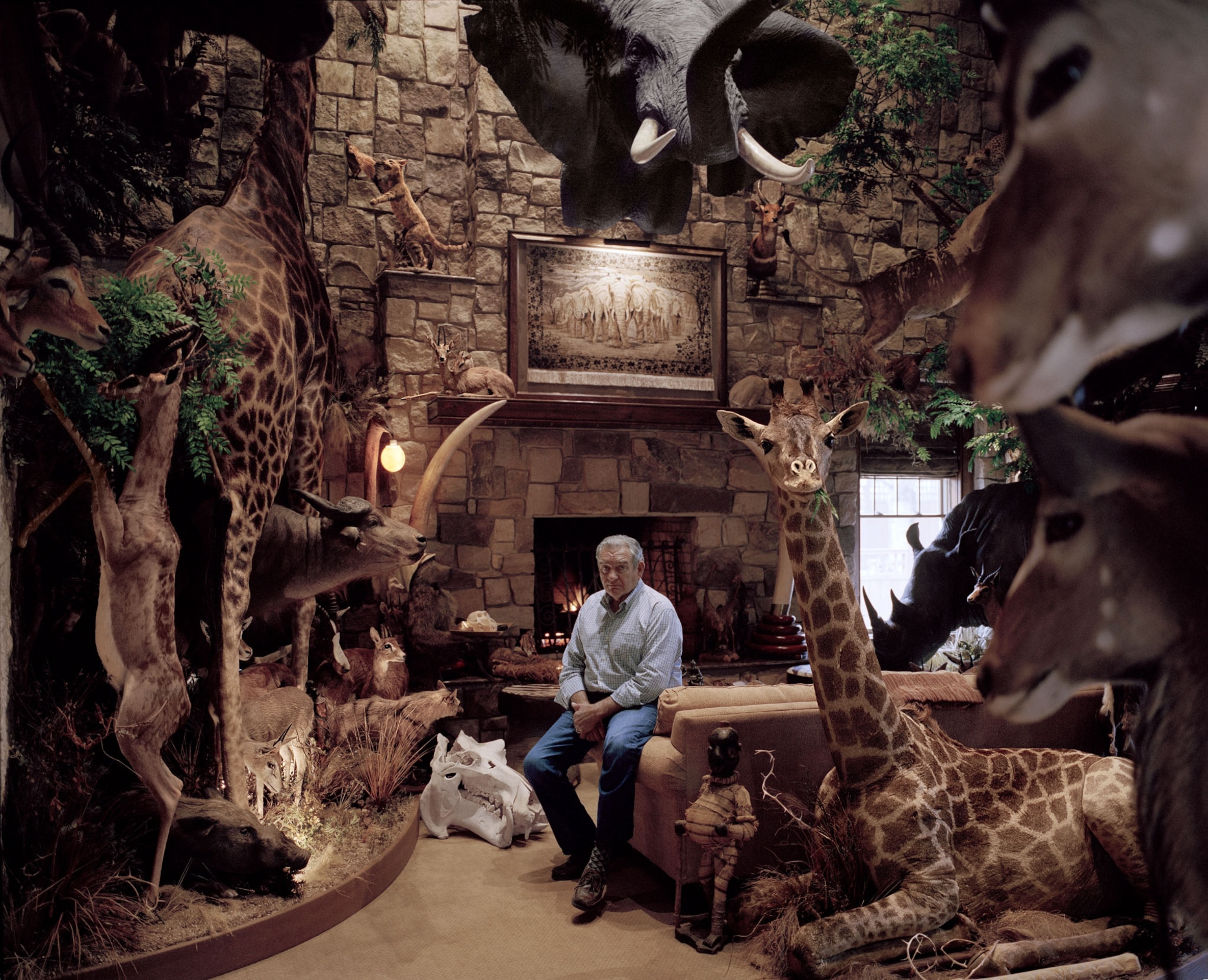 a man sitting before a fireplace in a room with man exotic taxidermy wild animals